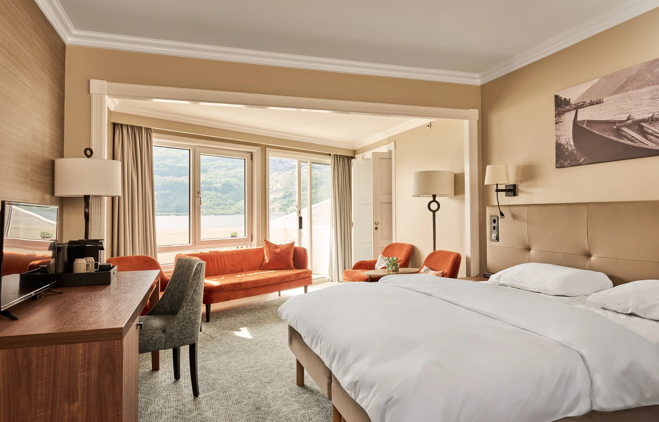 A hotel room with a large bed, orange chairs, and a window view of water and mountains.