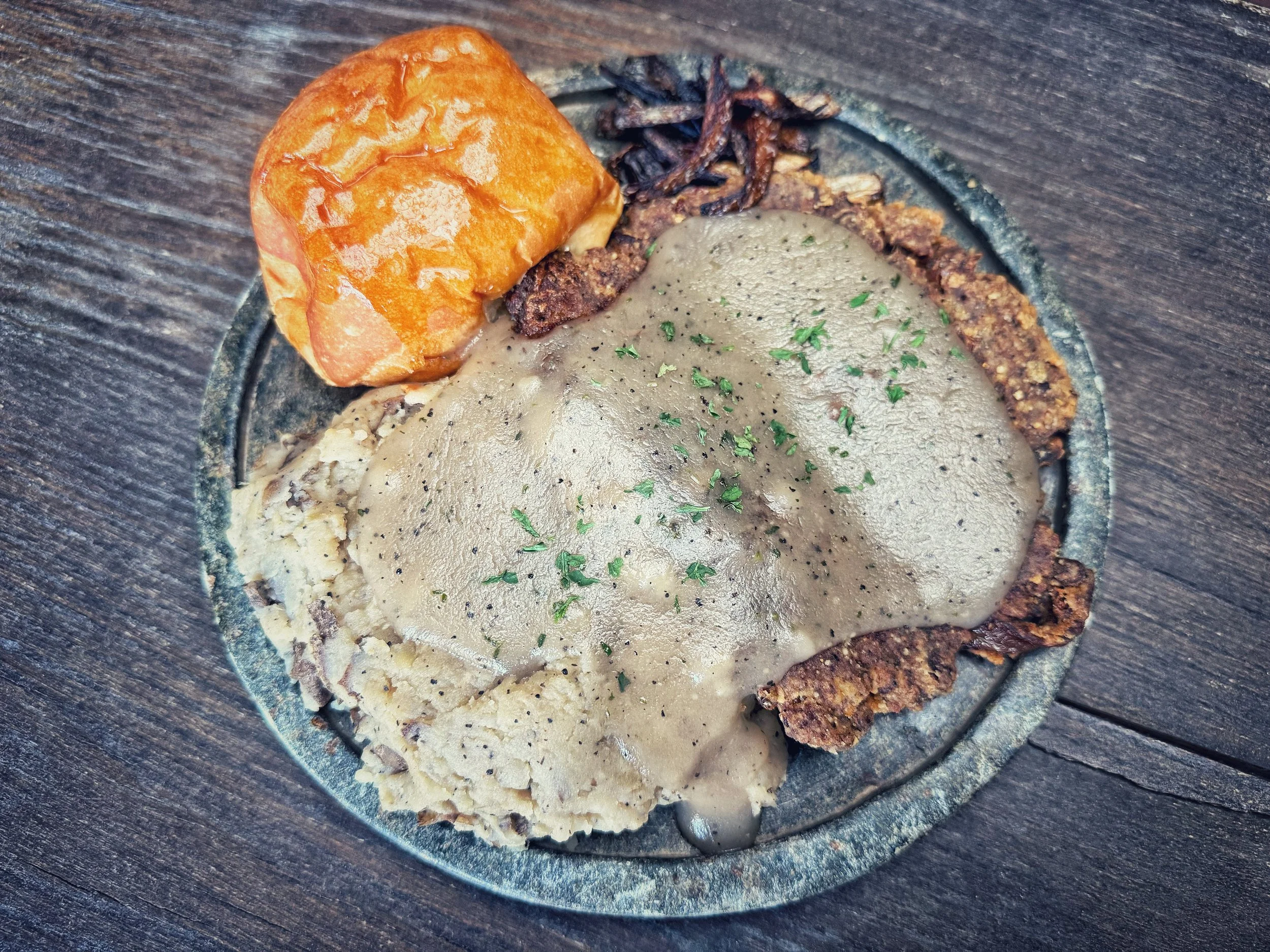 A plate of Mexican food featuring an enchilada topped with a gray mole sauce, a side of refried beans, and a roasted jalapeño pepper on a dark wooden table.