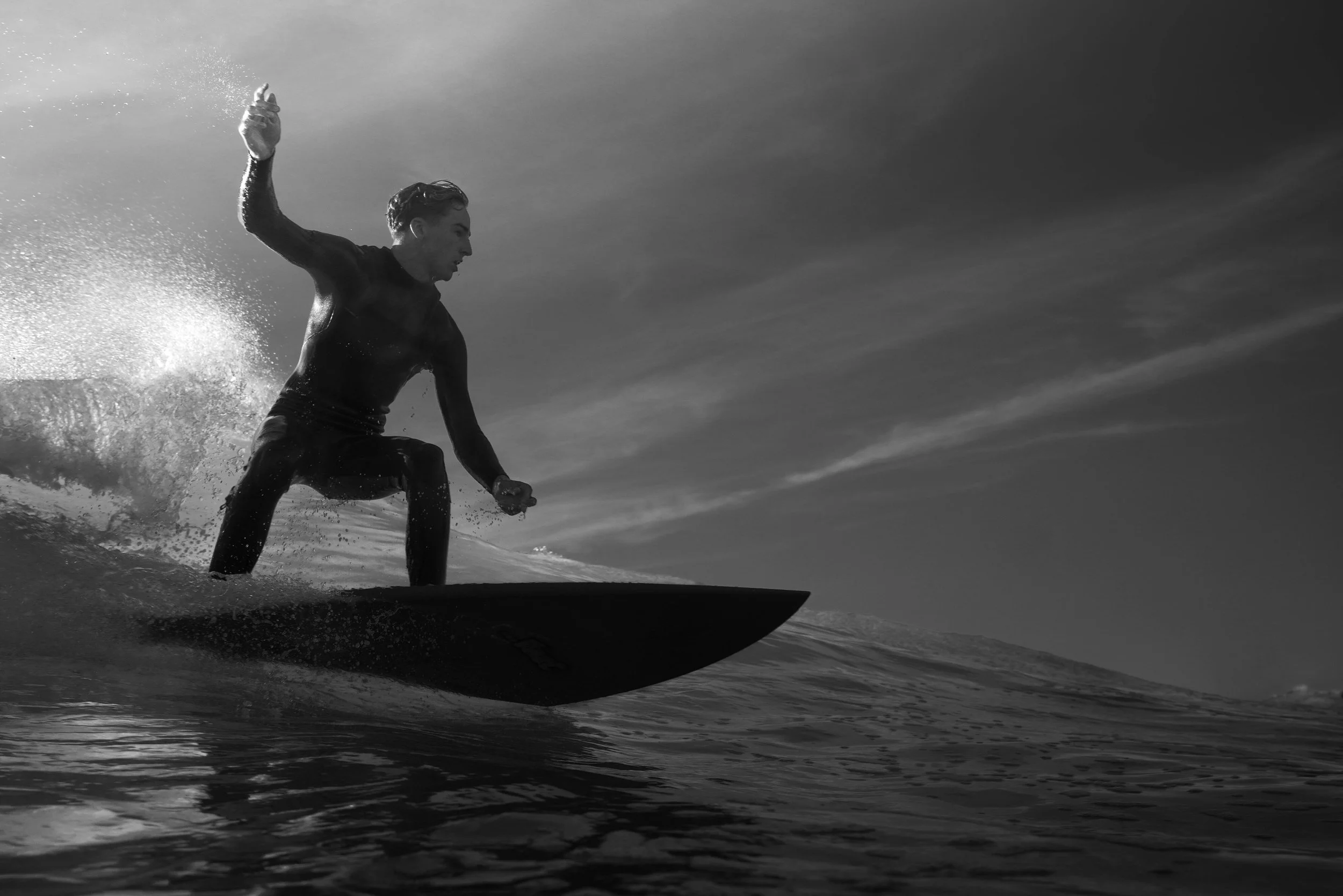 A person surfing on a wave in black and white, captured from a low angle with water splashing around them.
