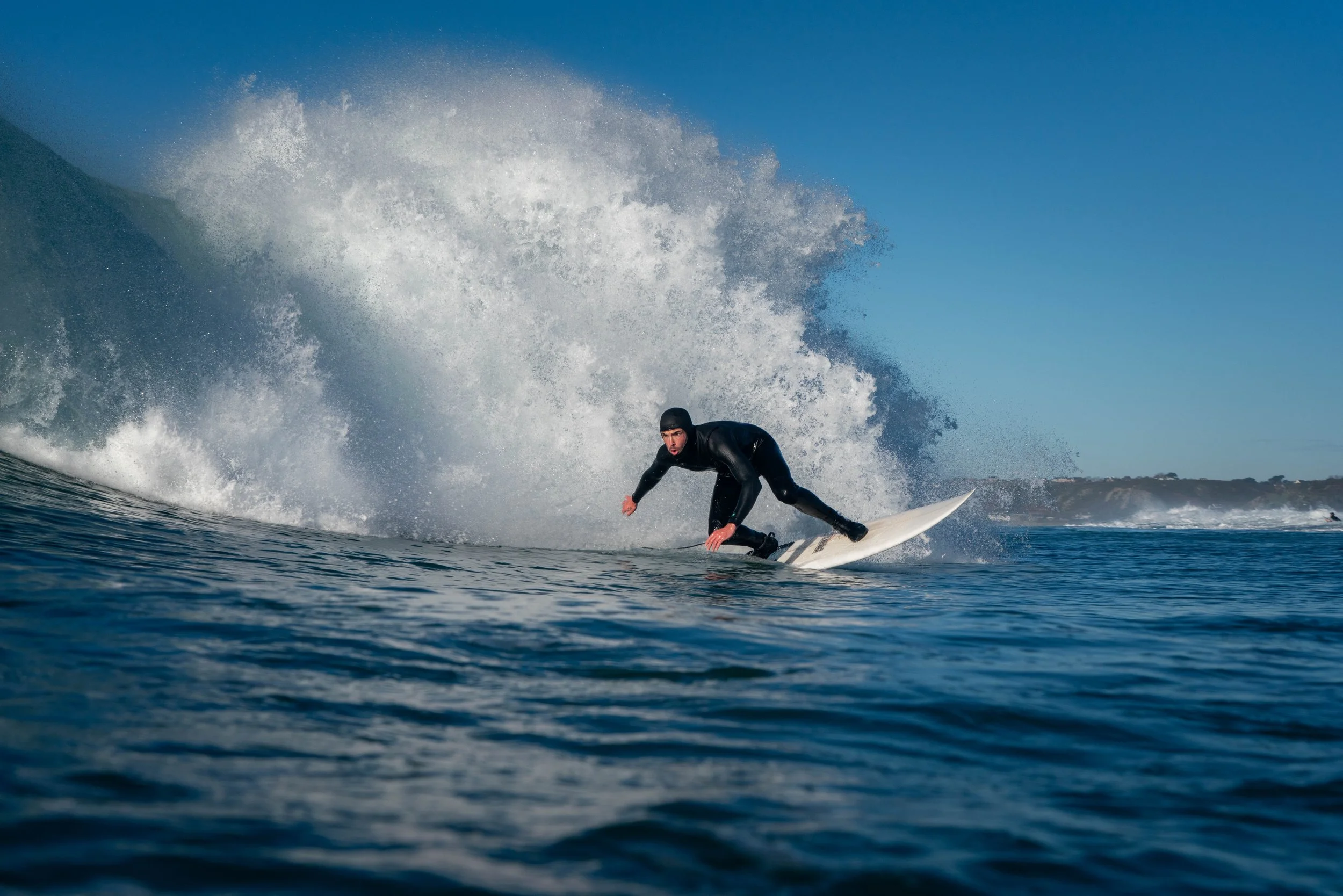 A male surfer in a black wetsuit riding a wave on a clear day with a blue sky.