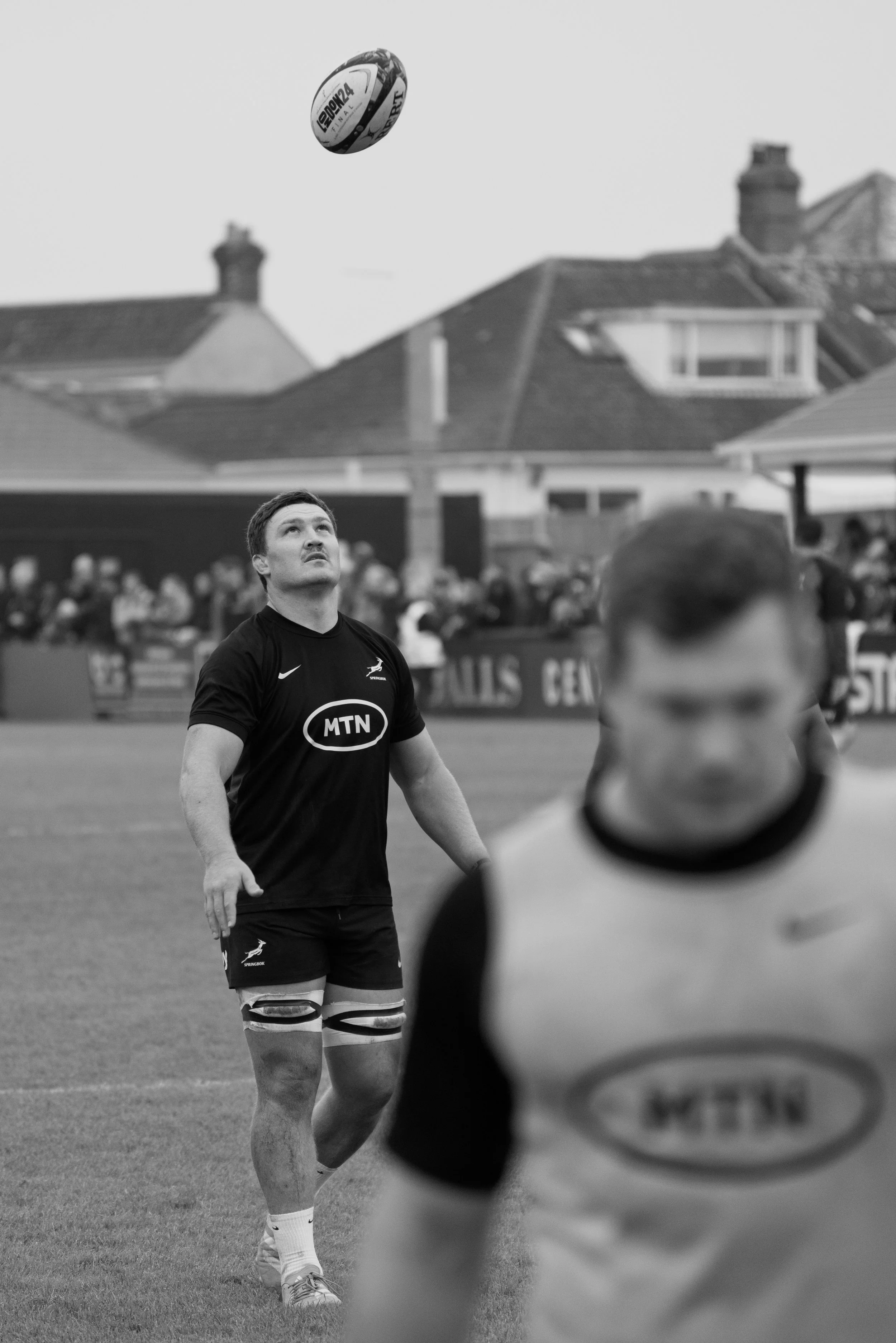 A South African rugby player in a black uniform looking at a rugby ball in the air during a game.