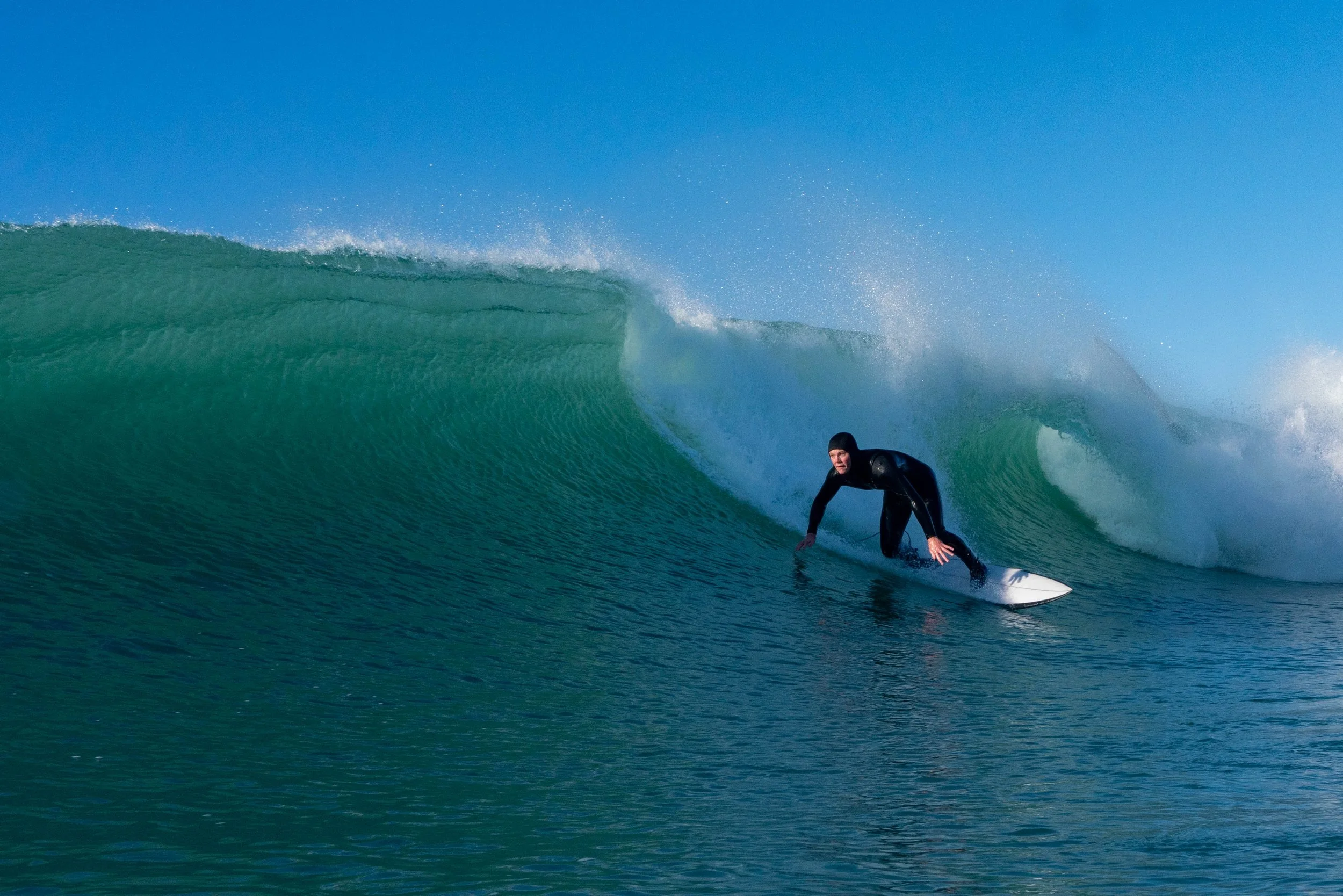 A person in a wetsuit surfing on a large wave under a clear blue sky.