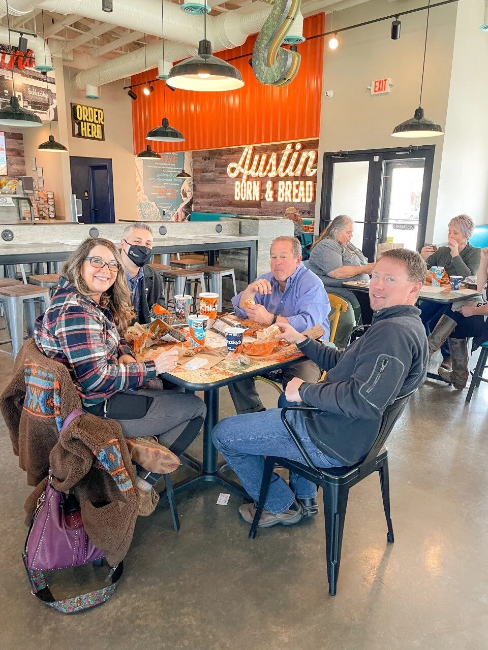 People sitting at a table in a restaurant with "Austin Born & Bread" neon sign."}