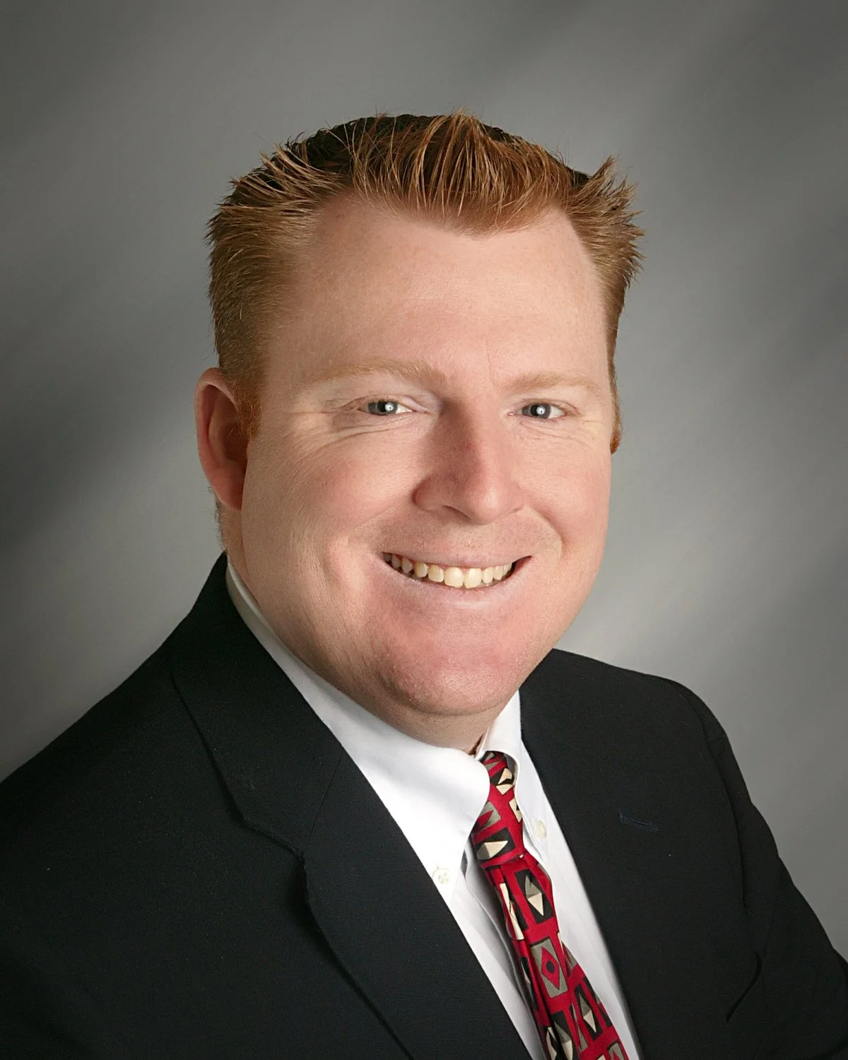 Portrait of a man in a suit and tie with a patterned background.