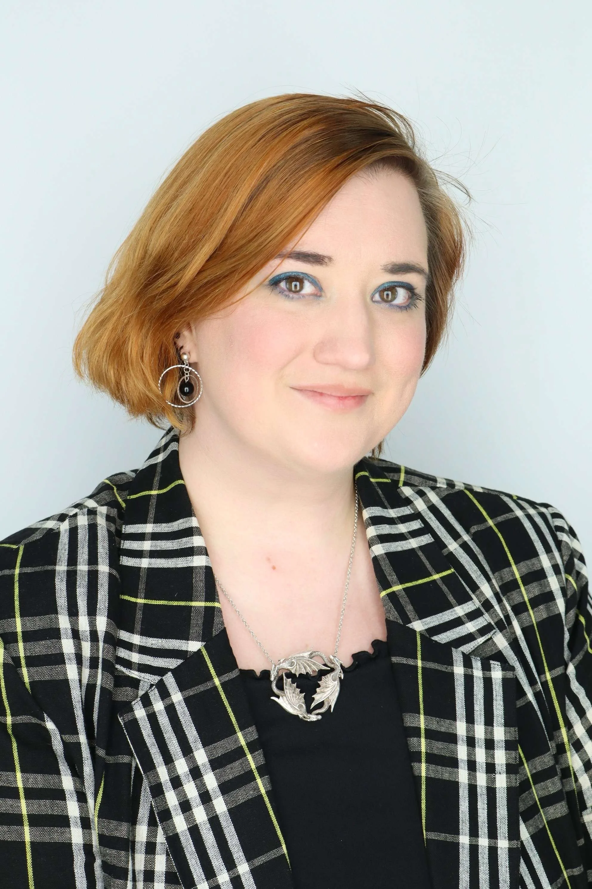 Smiling person against a gray background wearing a purple top and multi-colored striped jacket with short hair.