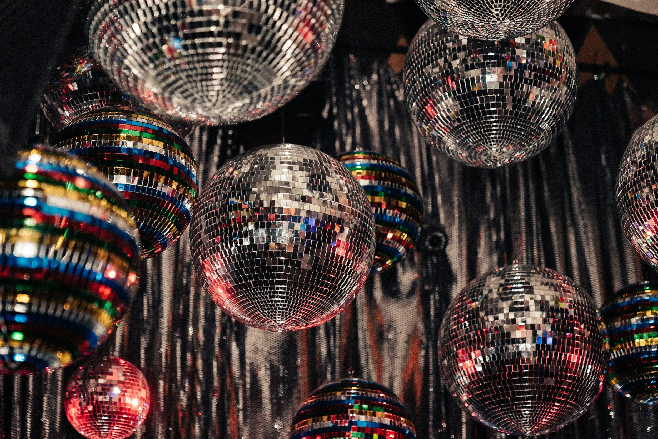 Multiple hanging disco balls with reflective mirror tiles in silver, multicolor, and rainbow patterns.