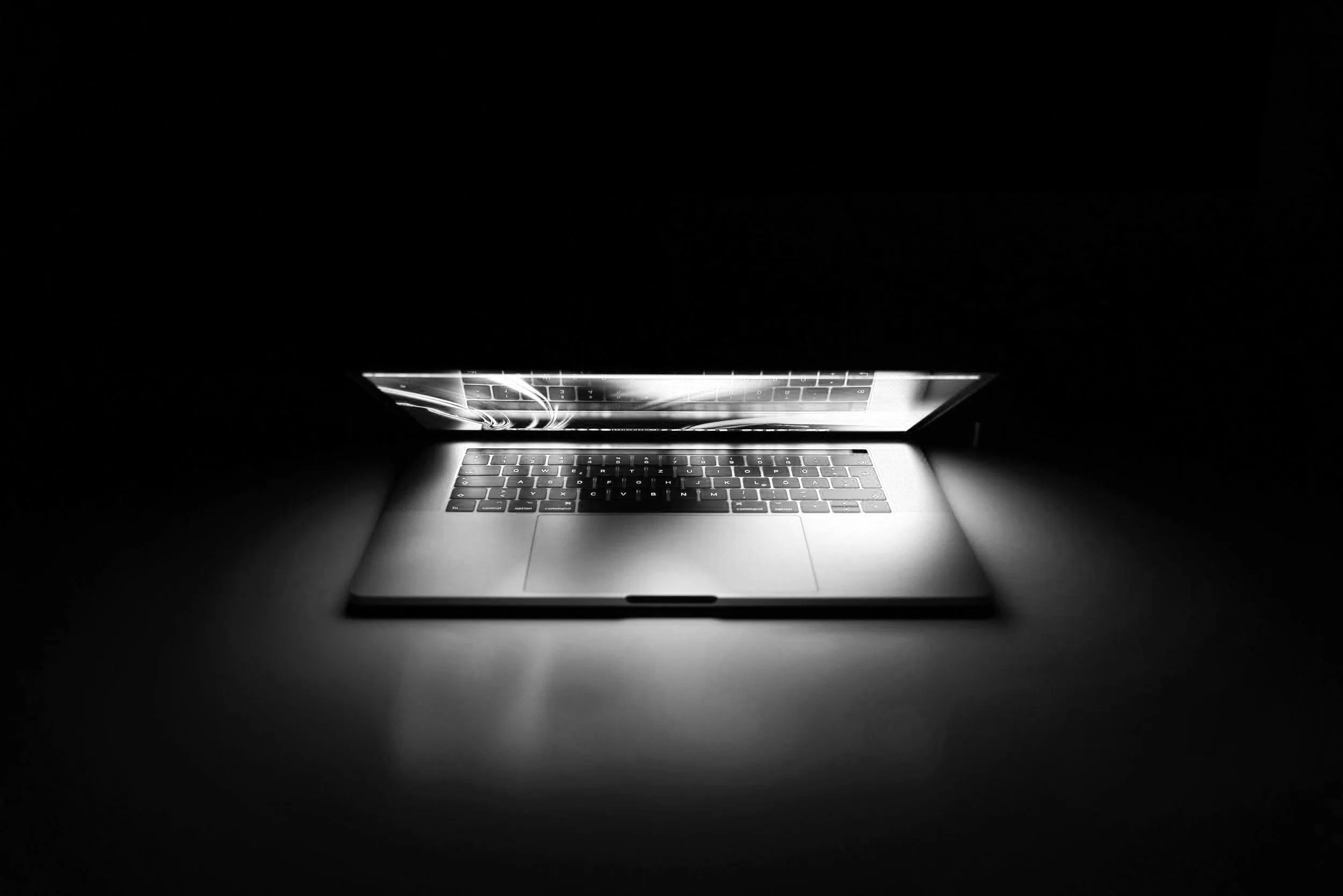 A laptop with a backlit keyboard in a dark room, projecting light onto the surrounding surface.