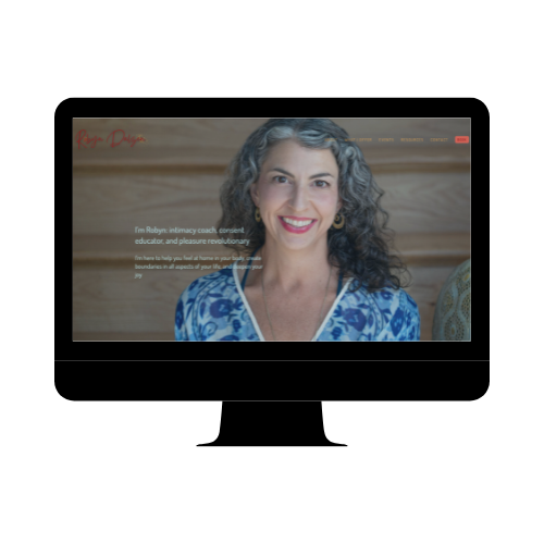 A woman with curly gray hair, smiling, wearing a blue patterned top, standing in front of a wooden background.