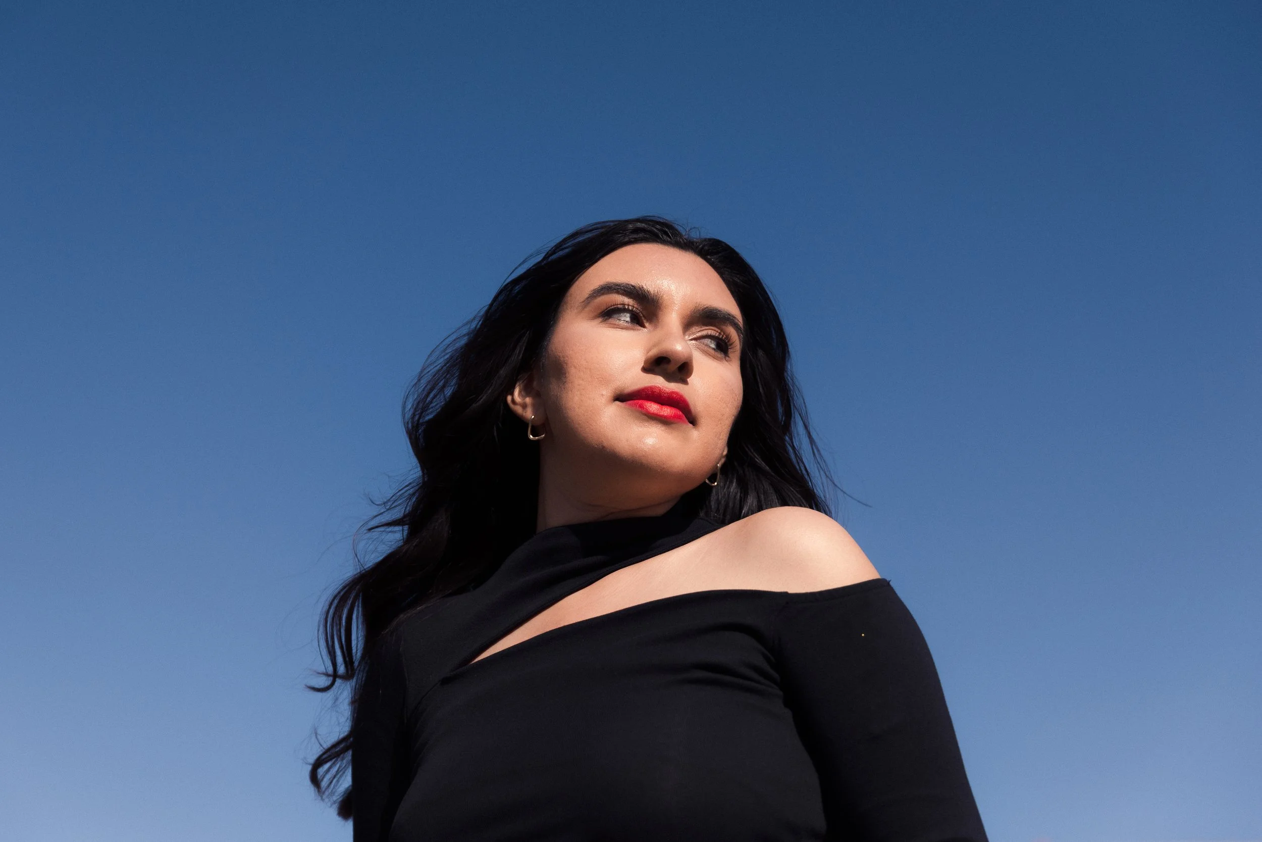Photoshoot in the Marais, Paris, France Photography by Owen Clarke.  Photo is of a women wearing a black top standing against a clear blue sky