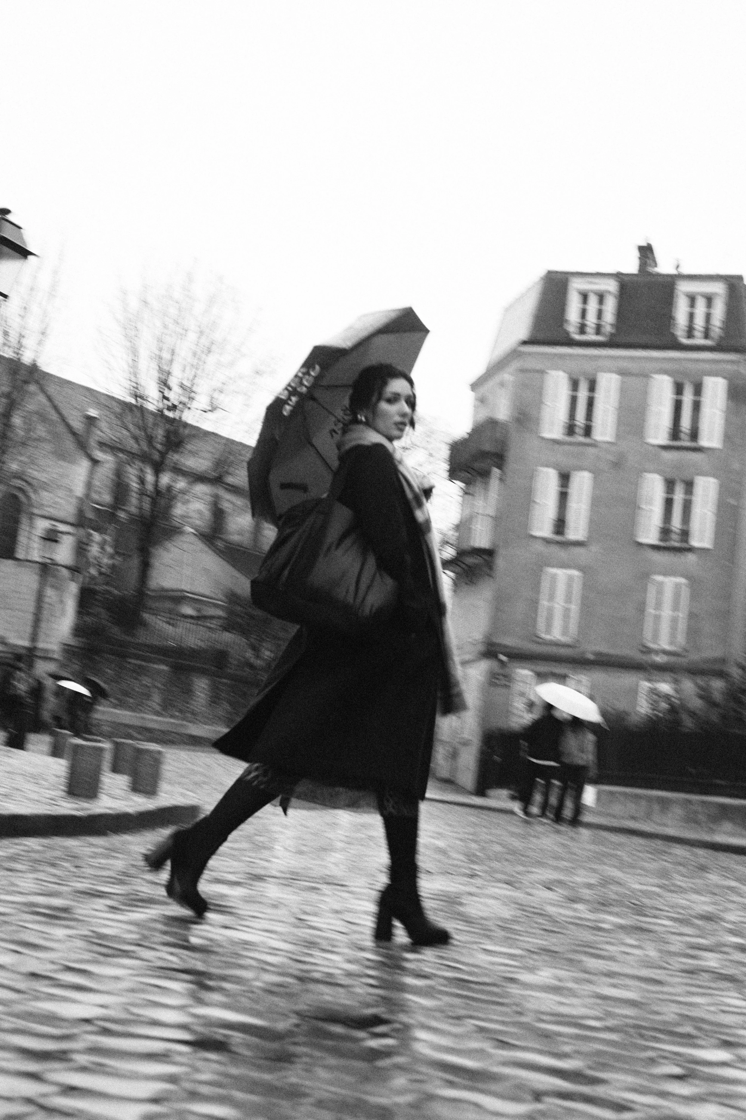 Photo shoot in Montmartre, Paris during February 2026. Photography by Owen Clarke. The photo is black and white, the person is wearing a black coat, with an umbrella