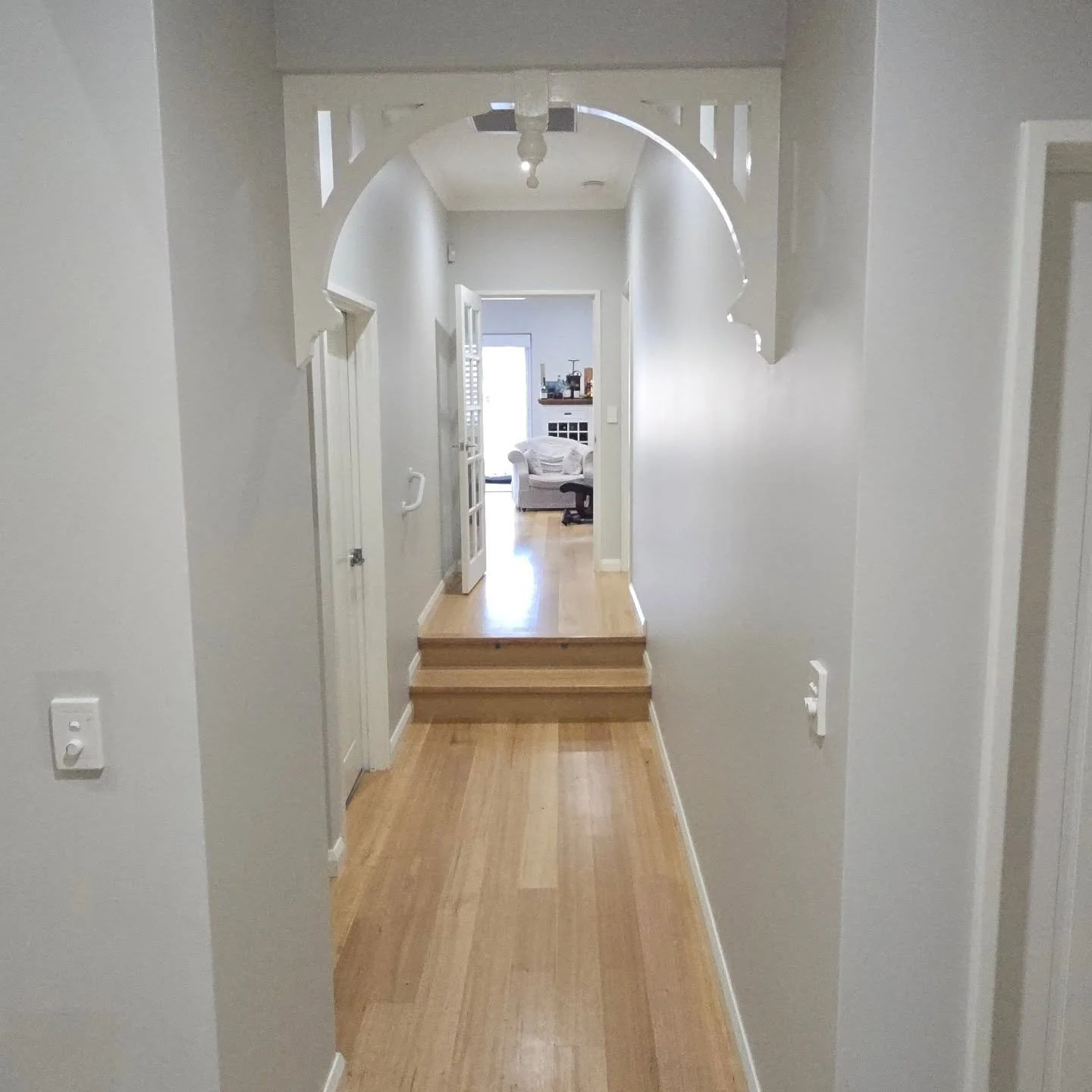 Long residential hallway in Salter Point with freshly painted light grey walls, polished timber flooring, and a decorative white timber archway.