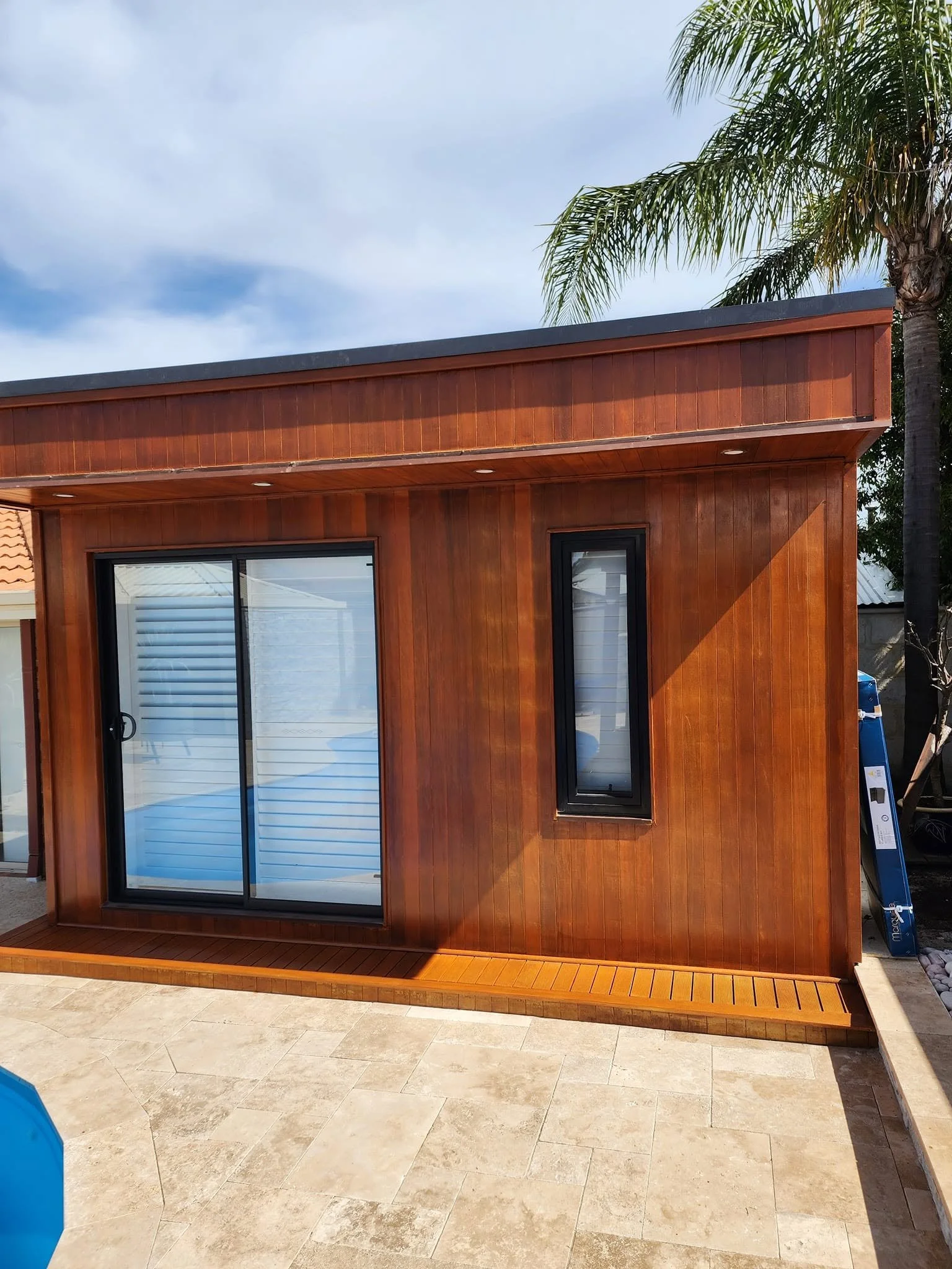 Fully restored and varnished timber pool studio featuring a deep wood stain and black-framed sliding glass doors.
