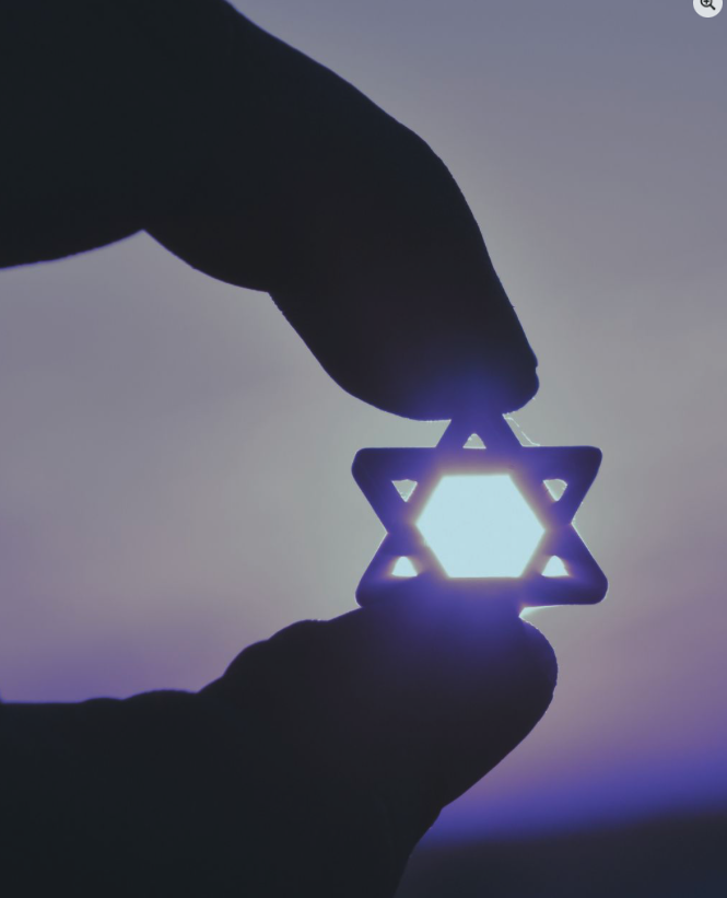 Hand holding a glowing Star of David ornament against a purple sky