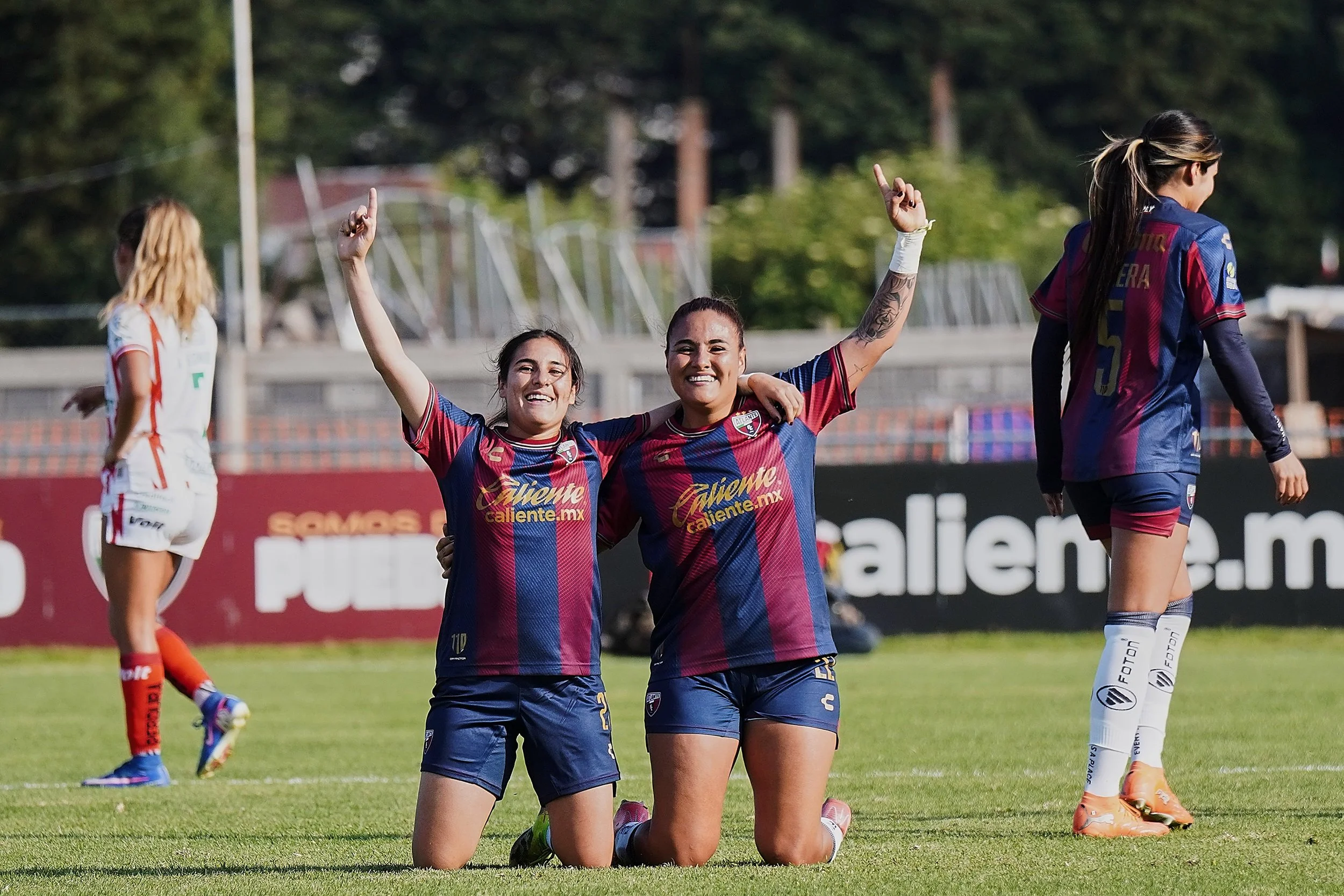 Judith Félix y Alexia Villanueva hincadas con un brazo apuntando al cielo sonríen