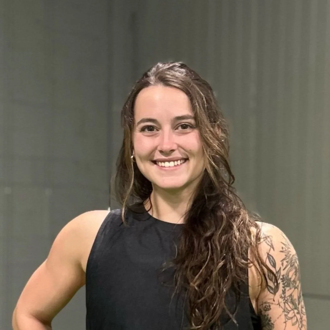 Smiling person with long hair wearing a 'Made2Move Physical Therapy' shirt; blurred indoor background.