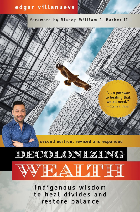 Book cover titled 'Decolonizing Wealth' by Edgar Villanueva. Features a cityscape with tall glass buildings, a man with arms crossed in front, and an eagle flying overhead. Includes a quote about healing and a yellow badge indicating it's the second revised edition.