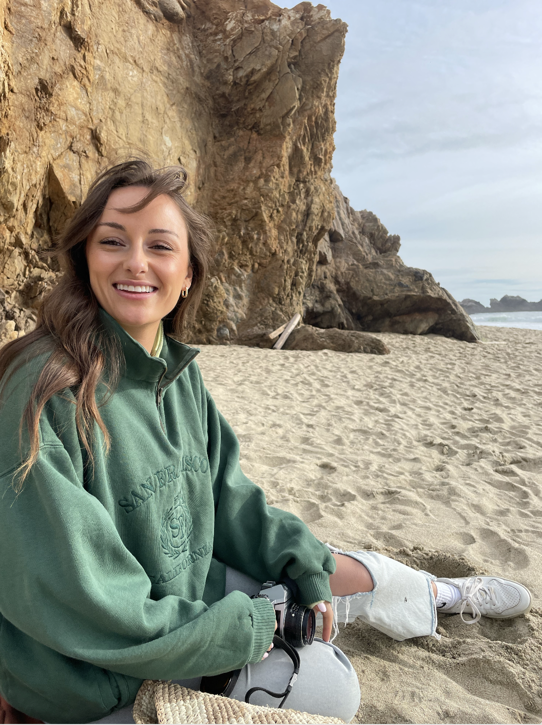 maddie parker sitting on the beach with her film camera in hand