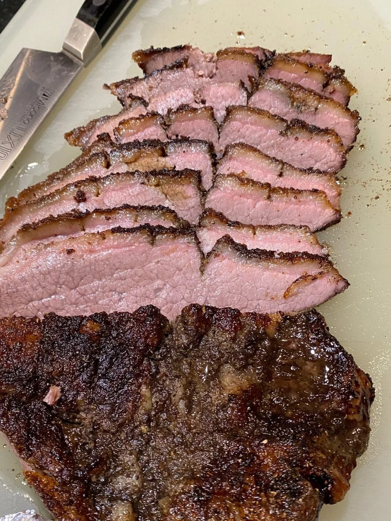 Perfectly cooked smoked beef brisket sliced on a white cutting board with a realistic bark crust.