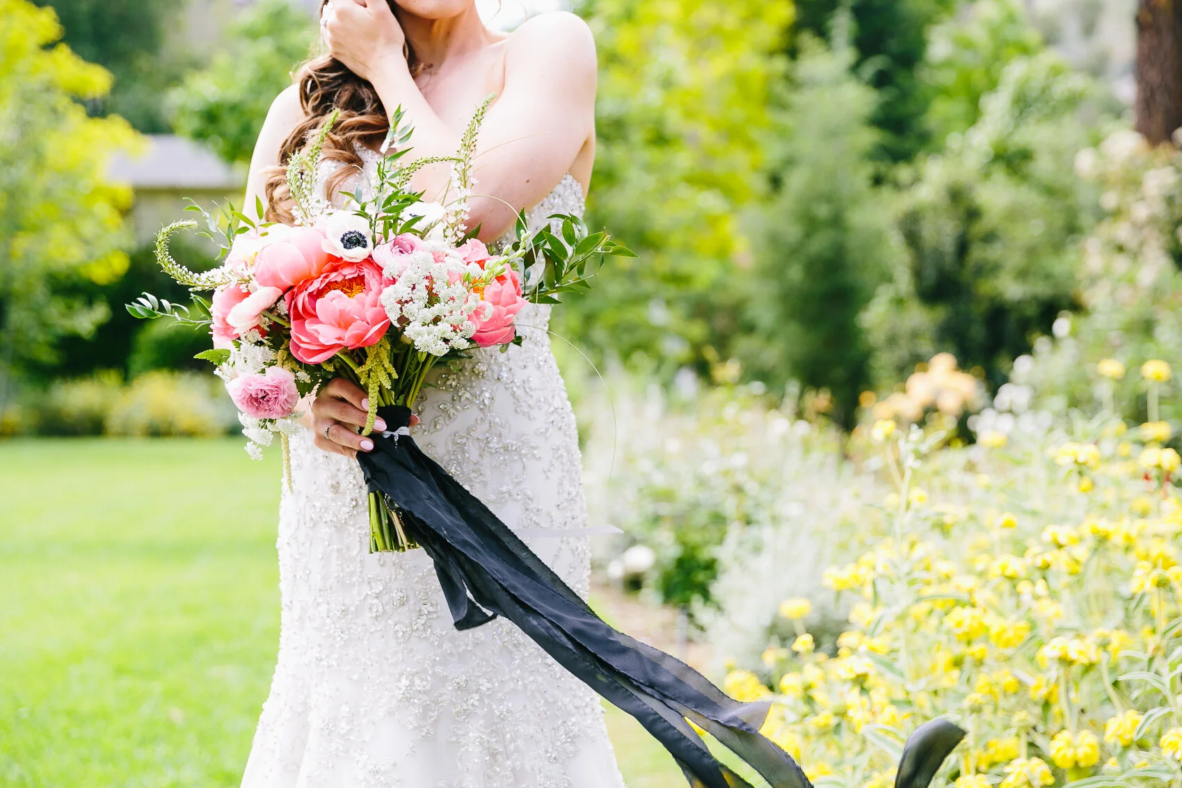 Bride holding colorful bouquet in a garden, wearing a white beaded wedding dress.