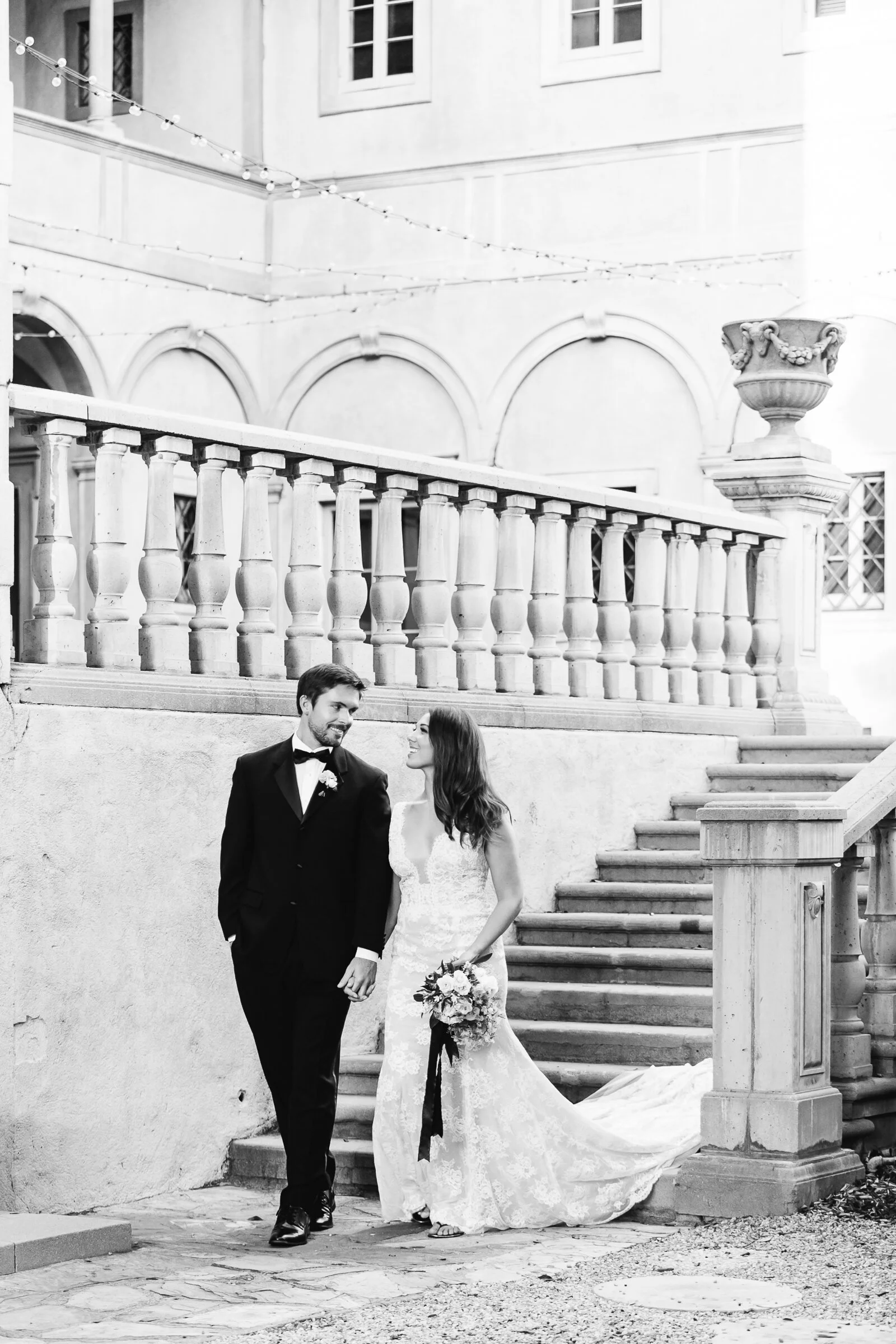 Bride and groom walking hand in hand in front of a vintage building with string lights.