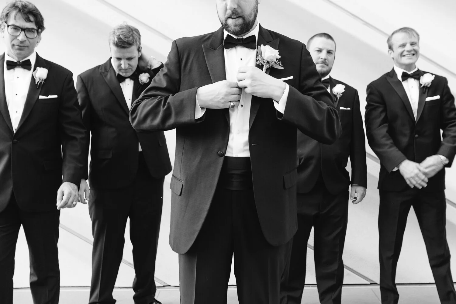 Groomsmen in tuxedos adjusting their jackets, preparing for a wedding.