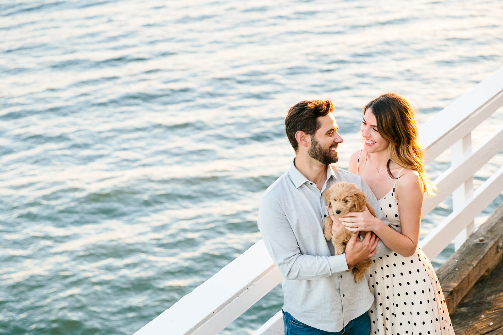 Couple holding a puppy on a pier with ocean in the background.