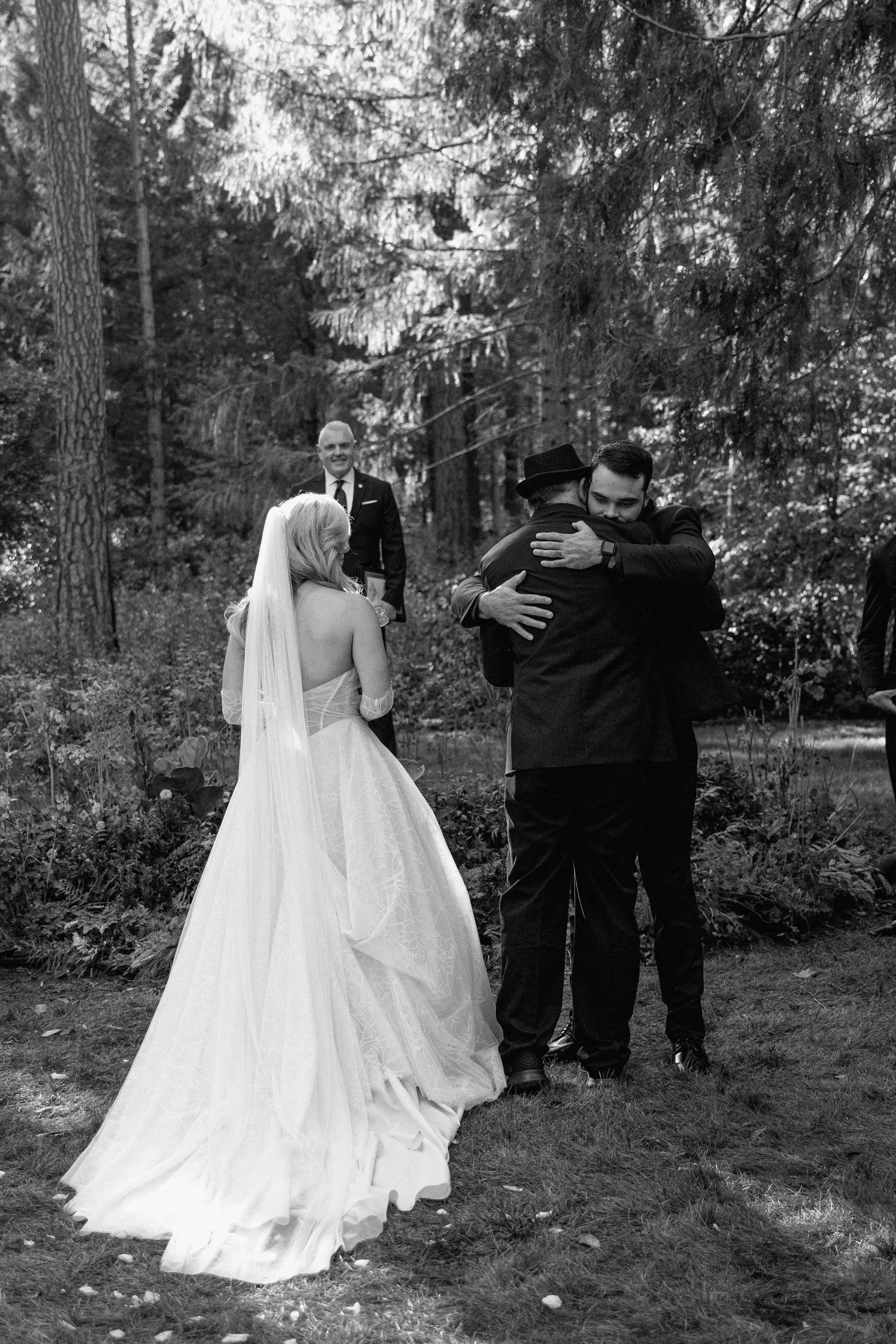 A black and white photo of a groom hugging bride's dad during the wedding ceremony