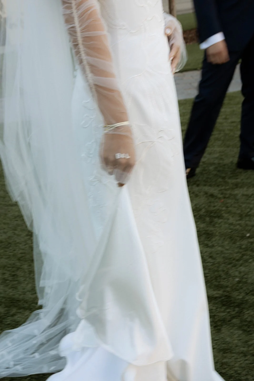 A blurry photo of a bride's wedding dress and embroidered gloves