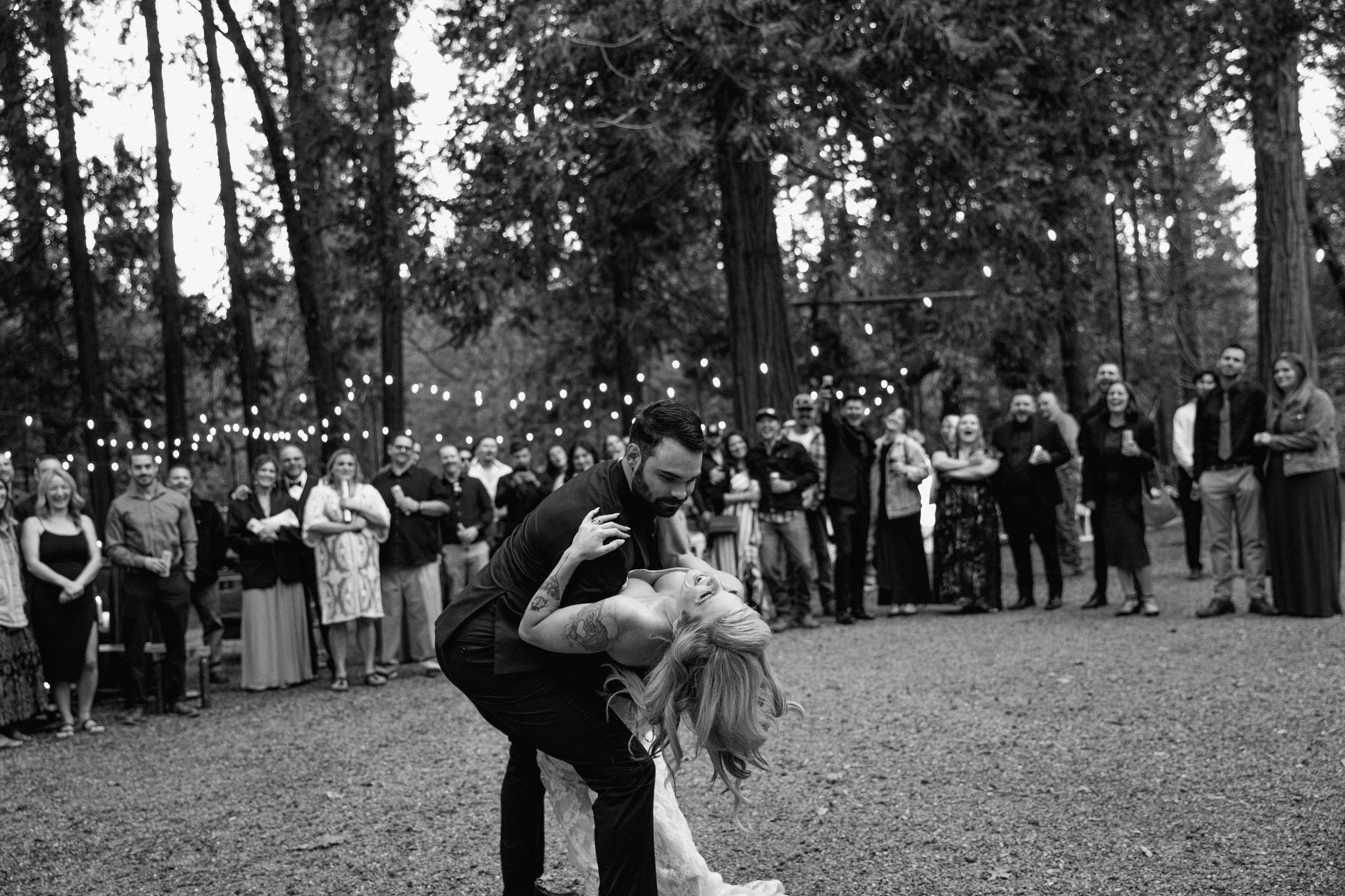 A black and white photo of a groom dipping his bride during a first dance in a forest California  wedding venue