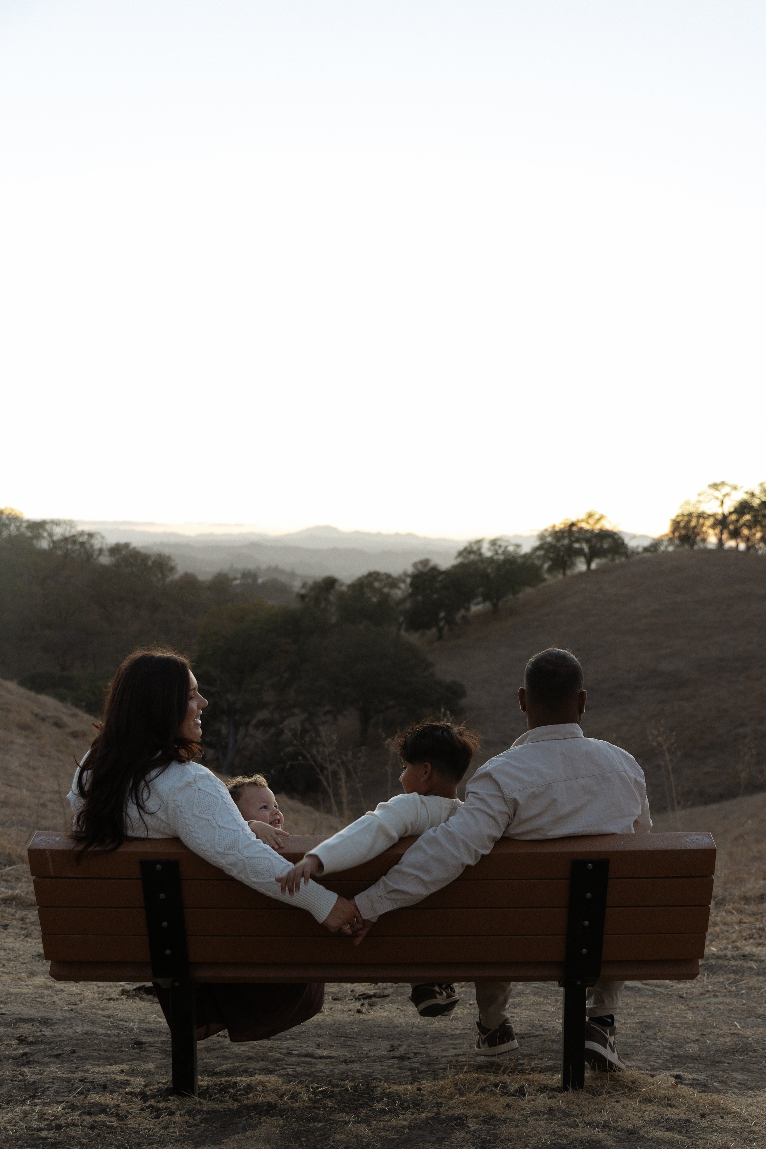 couple holds hands as kids interrupt their pda while sitting on a bench at the end of their family session