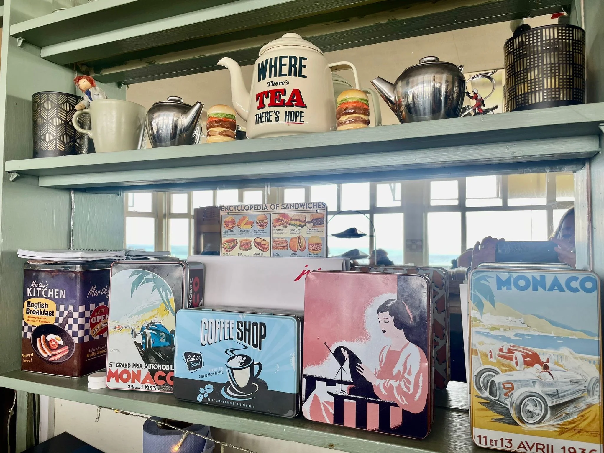 Shelf with a variety of vintage and retro-themed decorative tins and teapots, including designs related to tea, sandwiches, coffee