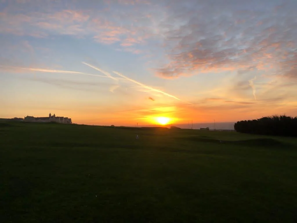 Sunset over a green landscape with a distant building silhouette and colorful sky.