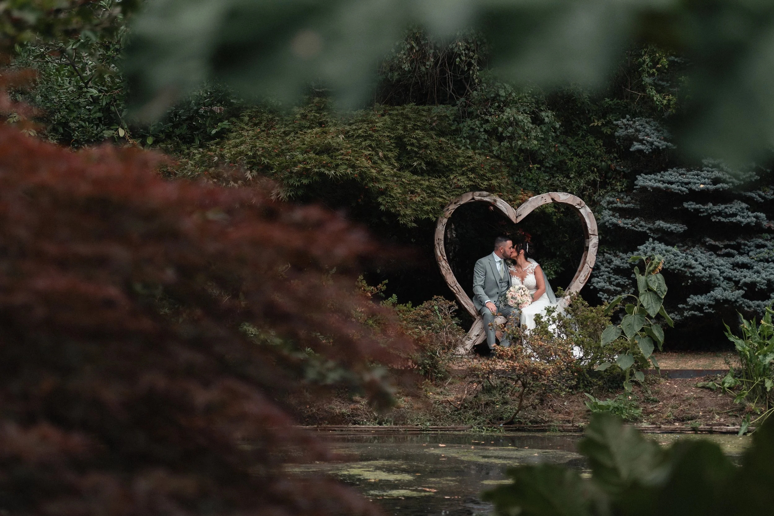 Rivervale Barn wedding with bride and groom kissing in a heart within the garden grounds. Rivervale Barn is a Hampshire wedding venue
