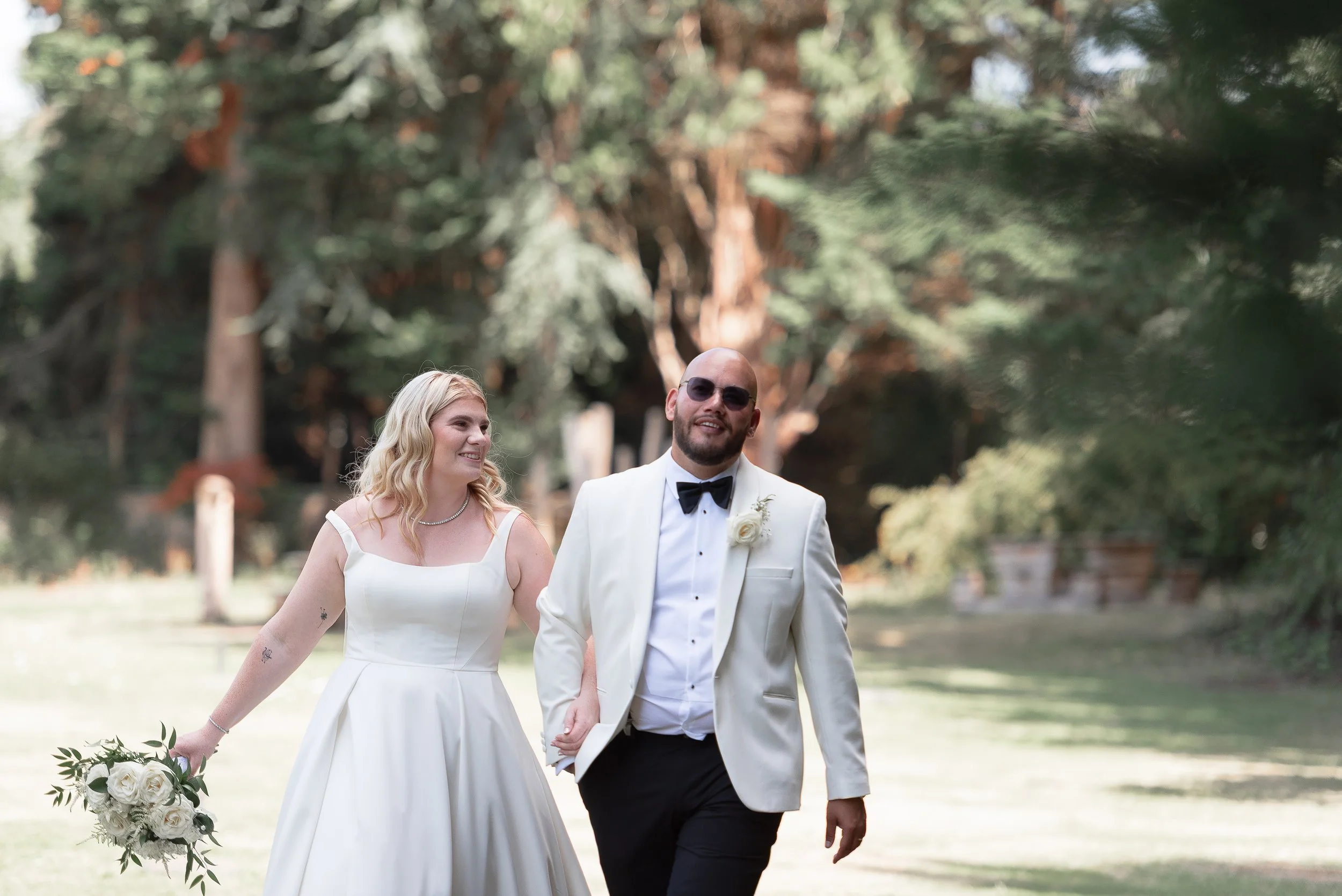 A bride and groom walking hand in hand outdoors, surrounded by greenery, during a wedding celebration in Basingstoke .
