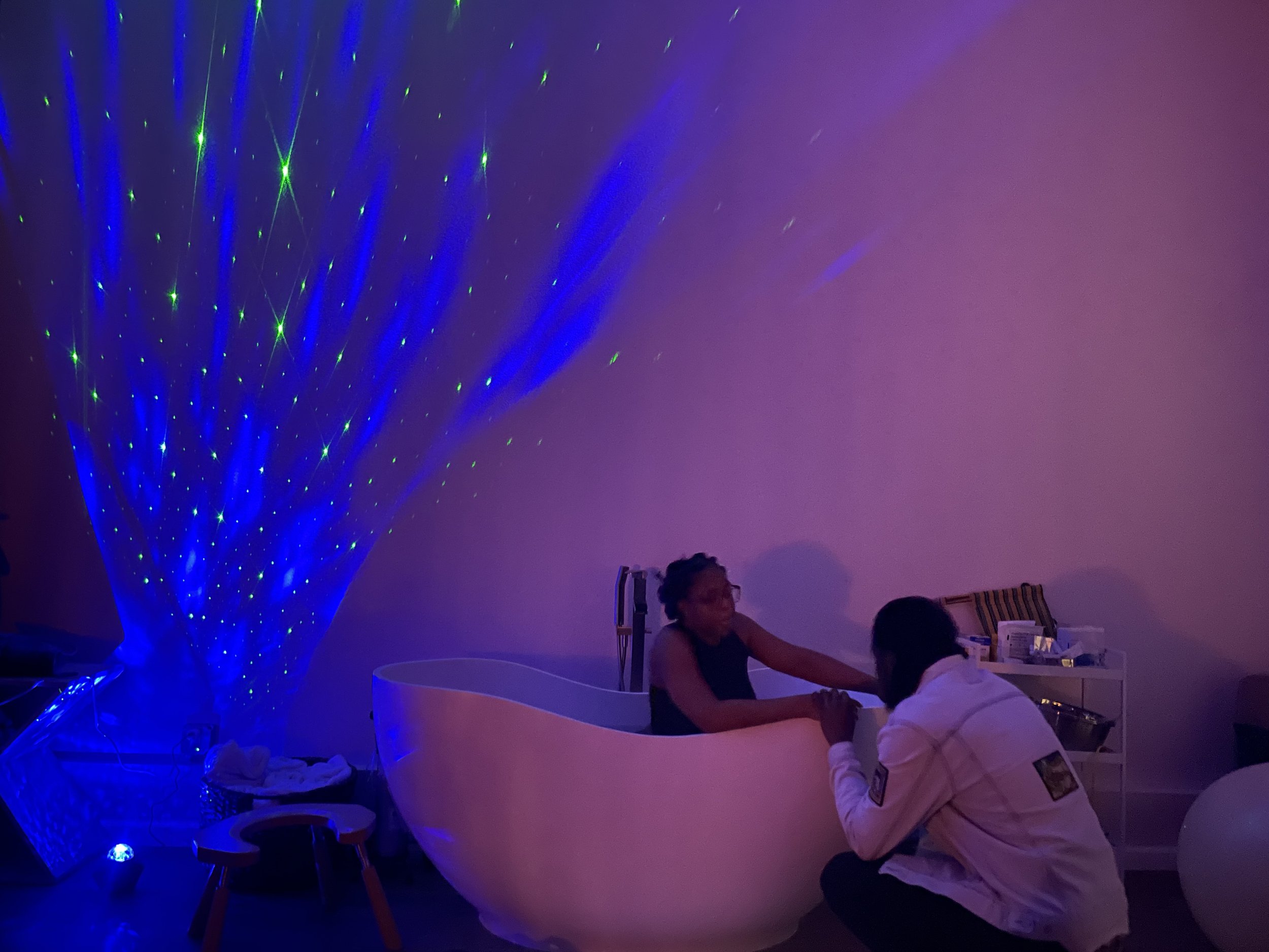 Group of people sitting around a white, curved table in a room illuminated with purple and blue laser lights, with a large blue laser light display on the wall.