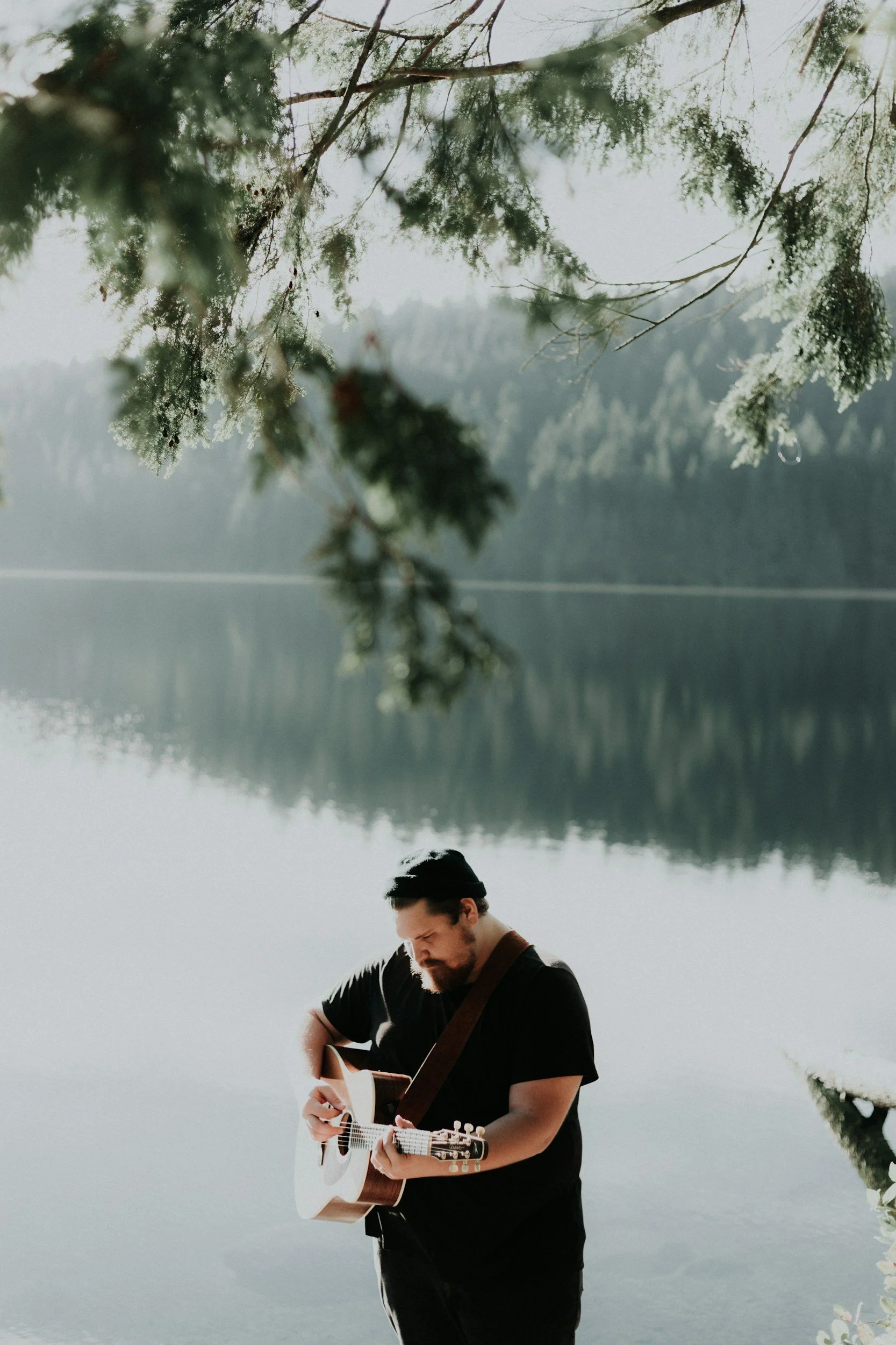 Musician playing guitar near a lake.