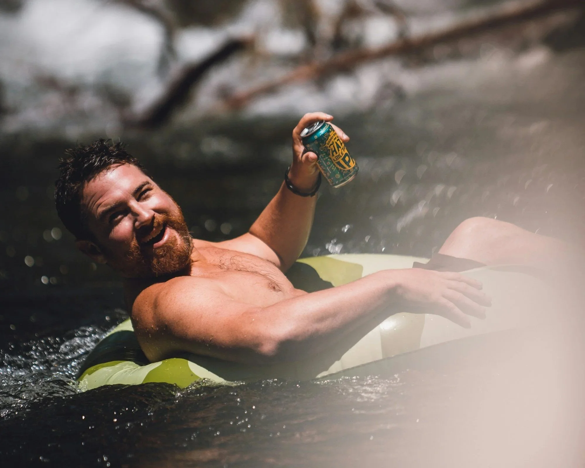 Man tubing on stony creek in the summer drinking a beer.