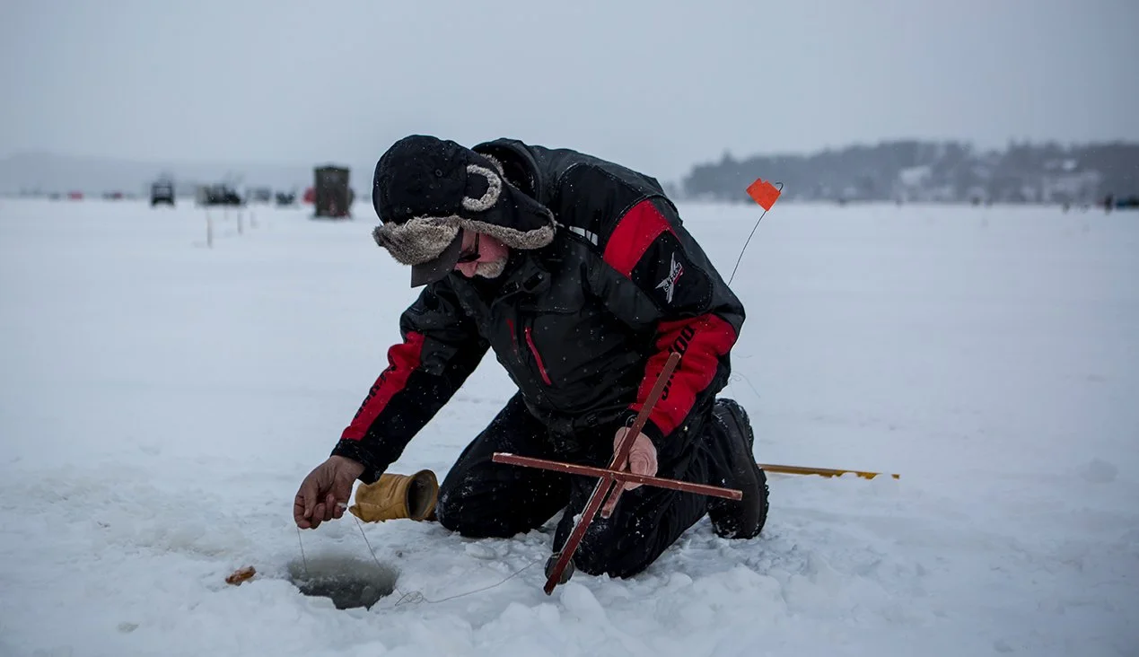 Man leaning over hole through the ice at the Northern Challenge Ice Fishing Derby.