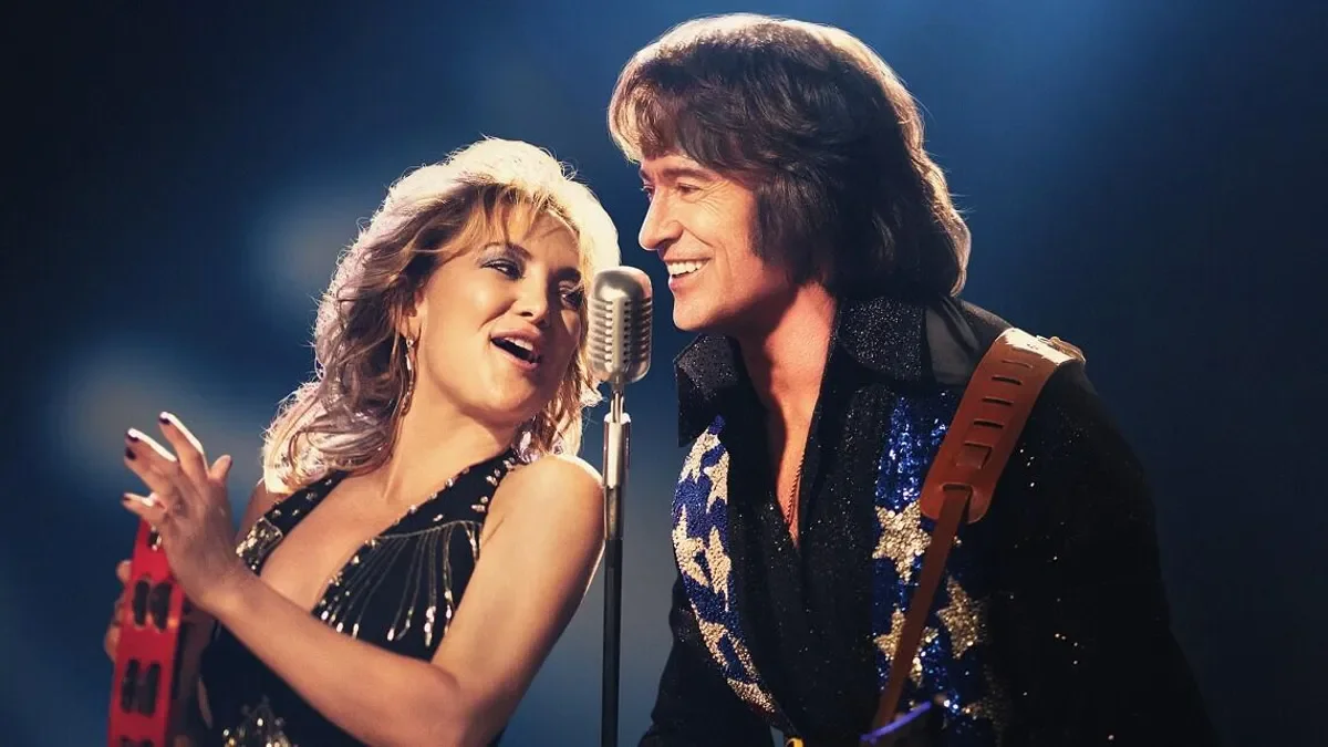 Kate Hudson playing the tambourine and singing with Hugh Jackman who also plays guitar in Song Sung Blue.