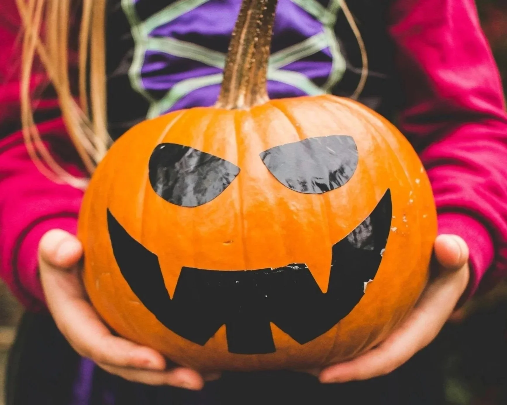 Girl in halloween costume holding a jack o'lantern.