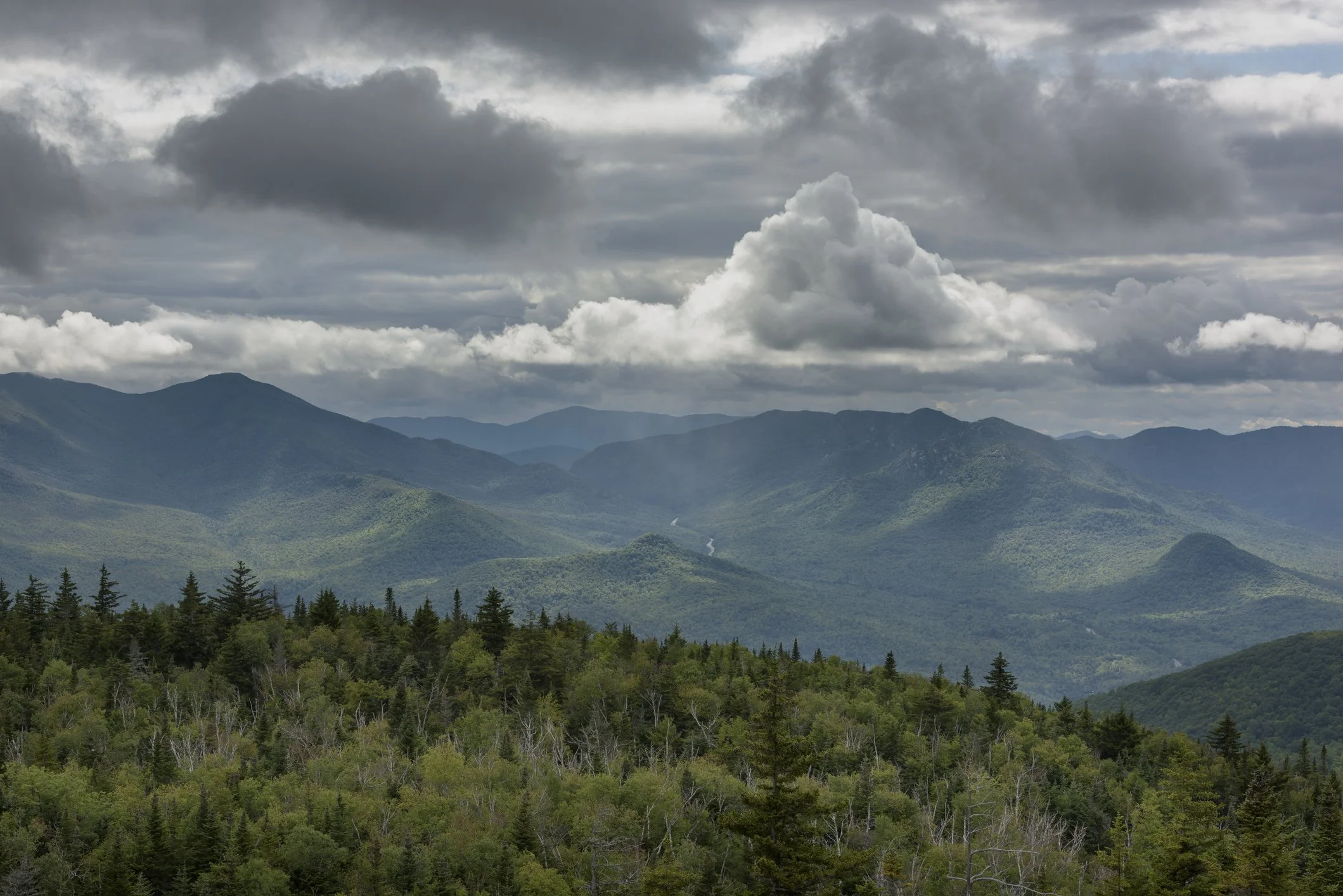 A dramatic sky of gray and white clouds with areas of rain coming down on the mountains of the Keene Valley in the Adirondack Park of New York State