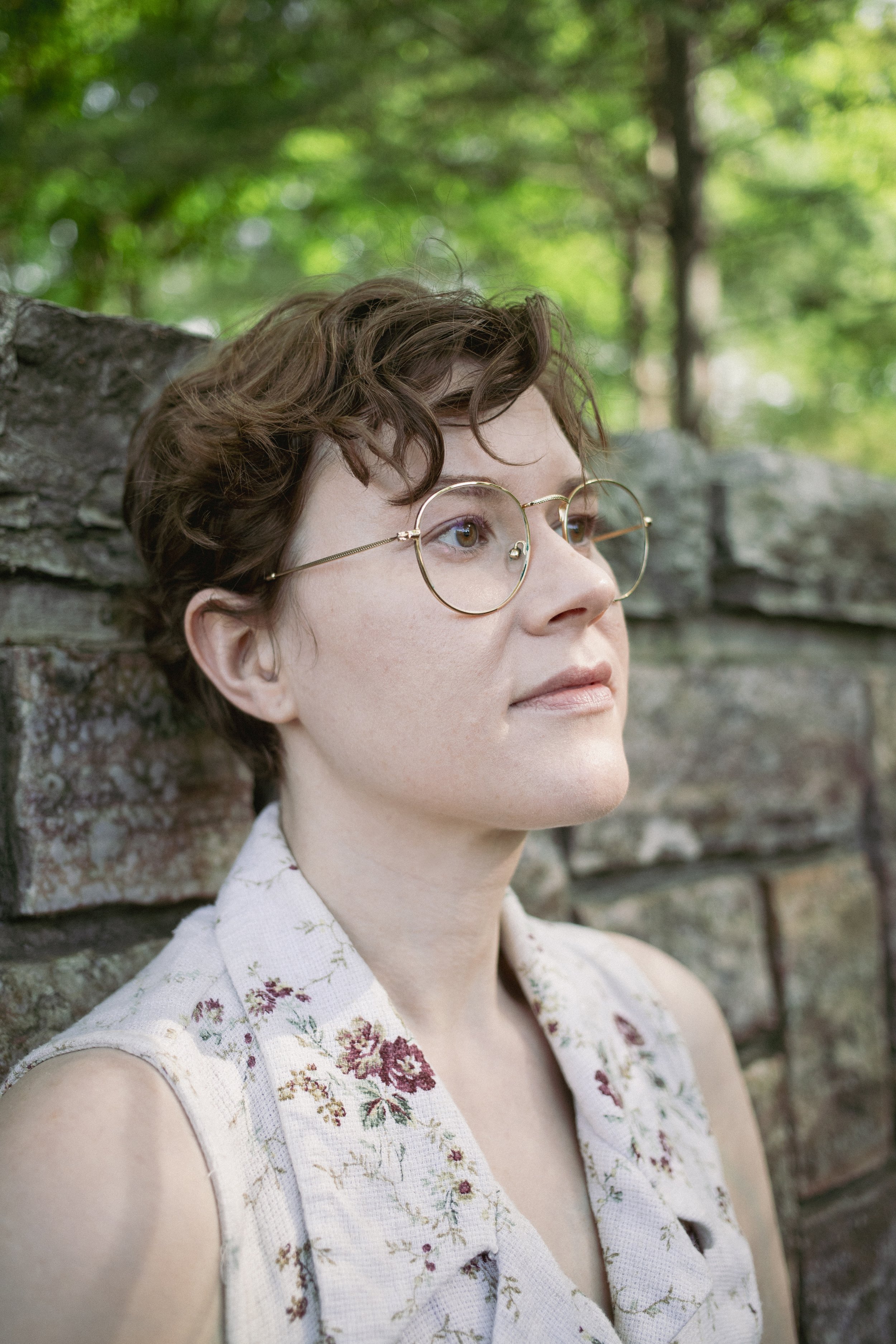Smiling, young white non-binary person with short, curly brown hair and glasses.