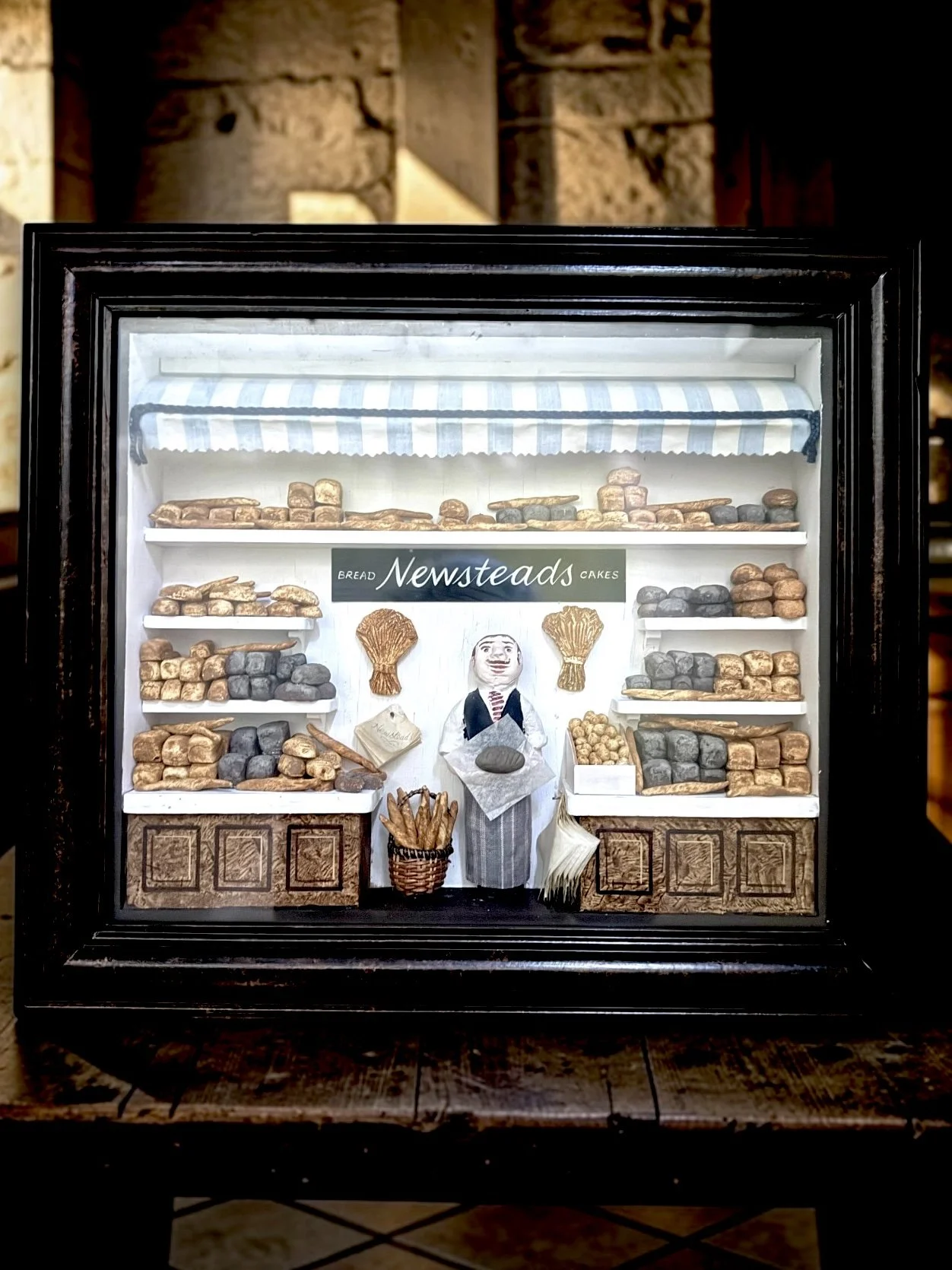 Newsteads Bakery Diorama
Twentieth-Century British Folk Art Bakery Diorama, Newsteads
Handcrafted dimensional folk art diorama depicting a traditional British bakery storefront interior with modeled breads, baskets, counters, signage, and baker figur