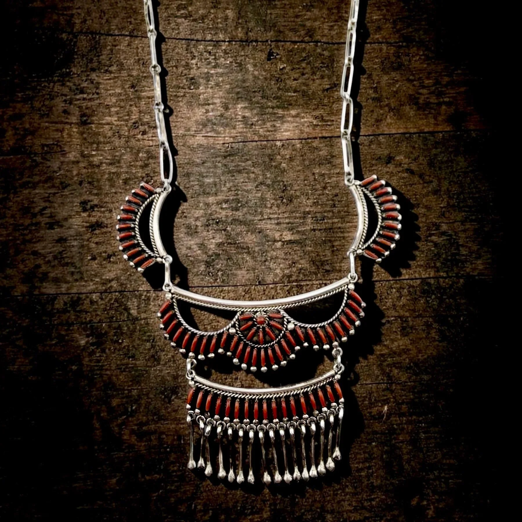 A silver necklace with orange beads and dangling silver ornaments is displayed on a dark wooden surface.