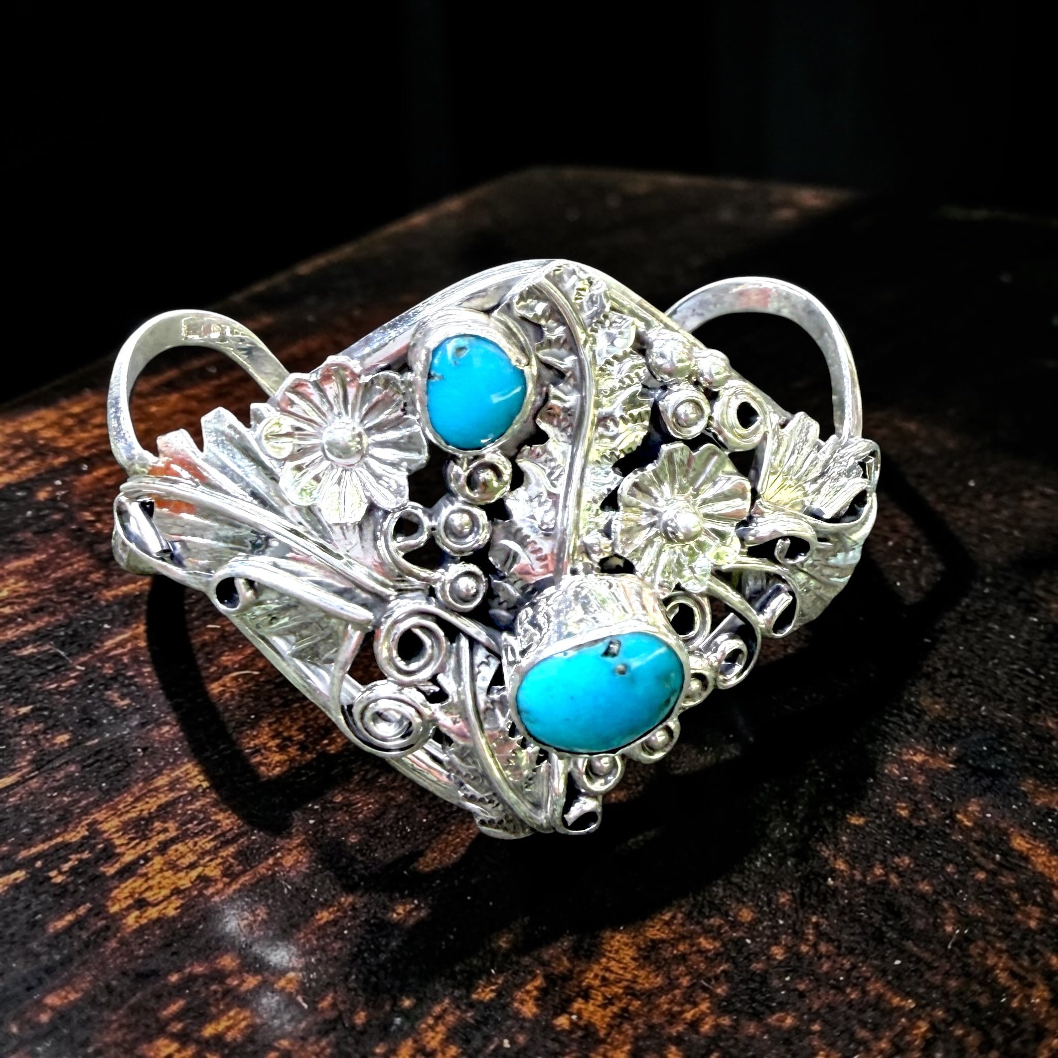 Signed HB  Y Sterling and Turquoise Floral Cuff
Two turquoise cabochons are surrounded by repoussé flowers, leaves, scrolls and applied silver elements