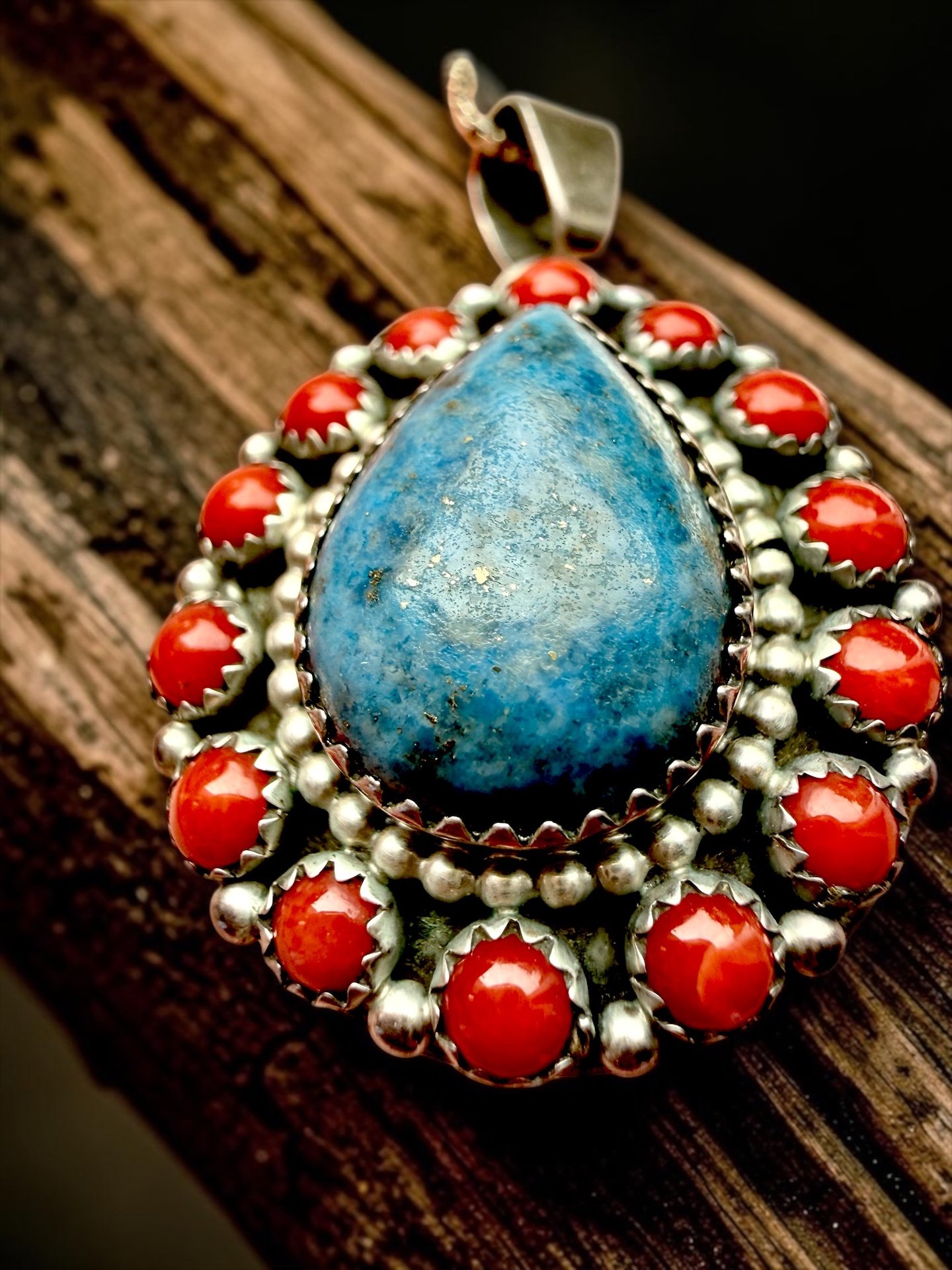 Close-up of a large turquoise stone jewelry piece with red coral and silver beads on a wooden surface.
