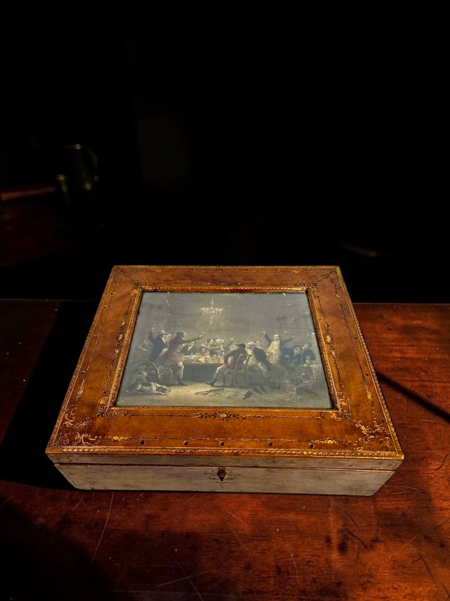 A. Förster Wien, Vienna, Austria, circa 1900, wood box wrapped in richly patinated brown leather, elaborate gilt-tooled foliate decoration, hinged lid with inset glass panel framing the hand-colored engraving “The Fox Hunter’s Toast,” original faded 