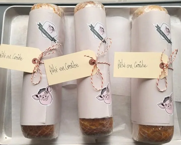 Brand Collateral: Le Petit Chapeau emblem stickers are applied directly to artisanal terrines wrapped in butcher paper. The nostalgic packaging is secured with red-and-white baker's twine and anchored by a vintage manila tag featuring handwritten lab
