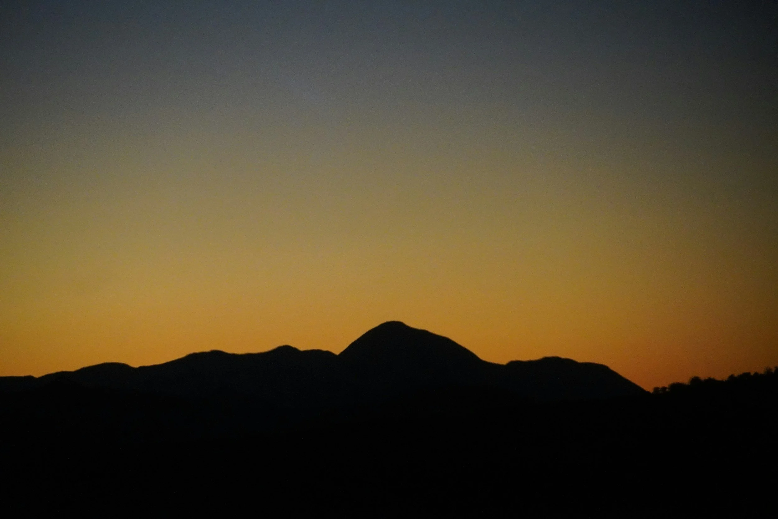 Silhouette of mountain range at sunset with gradient sky transitioning from yellow near horizon to dark blue at the top.