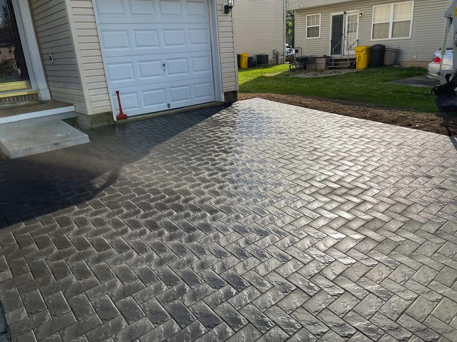 Newly paved driveway with brick pattern, some sections still wet, in front of a garage and house with steps leading to the door.